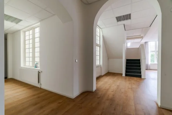 Licht en ruim interieur met houten vloer, grote ramen en een trap in een pand aan het Lange Voorhout.