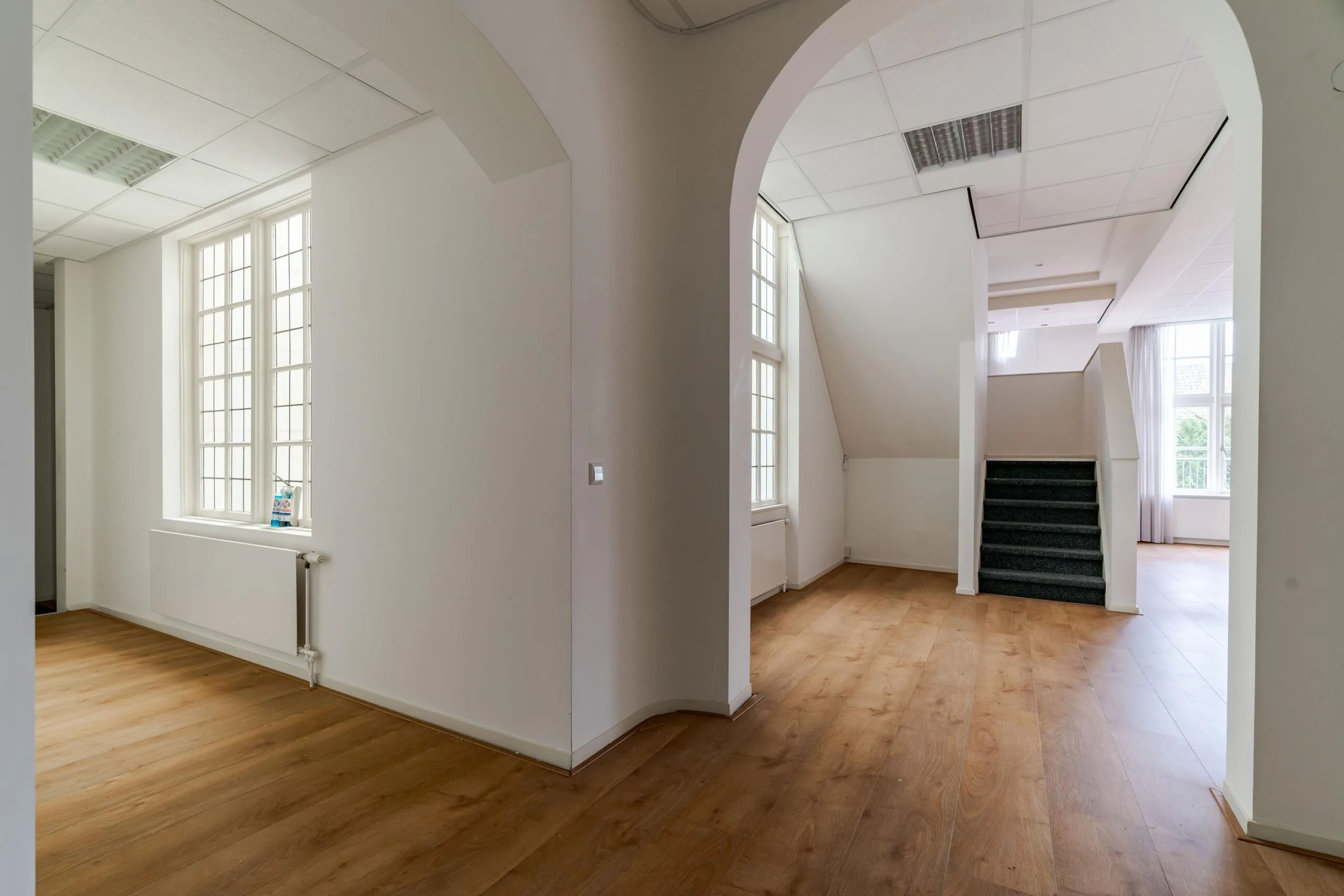 Licht en ruim interieur met houten vloer, grote ramen en een trap in een pand aan het Lange Voorhout.