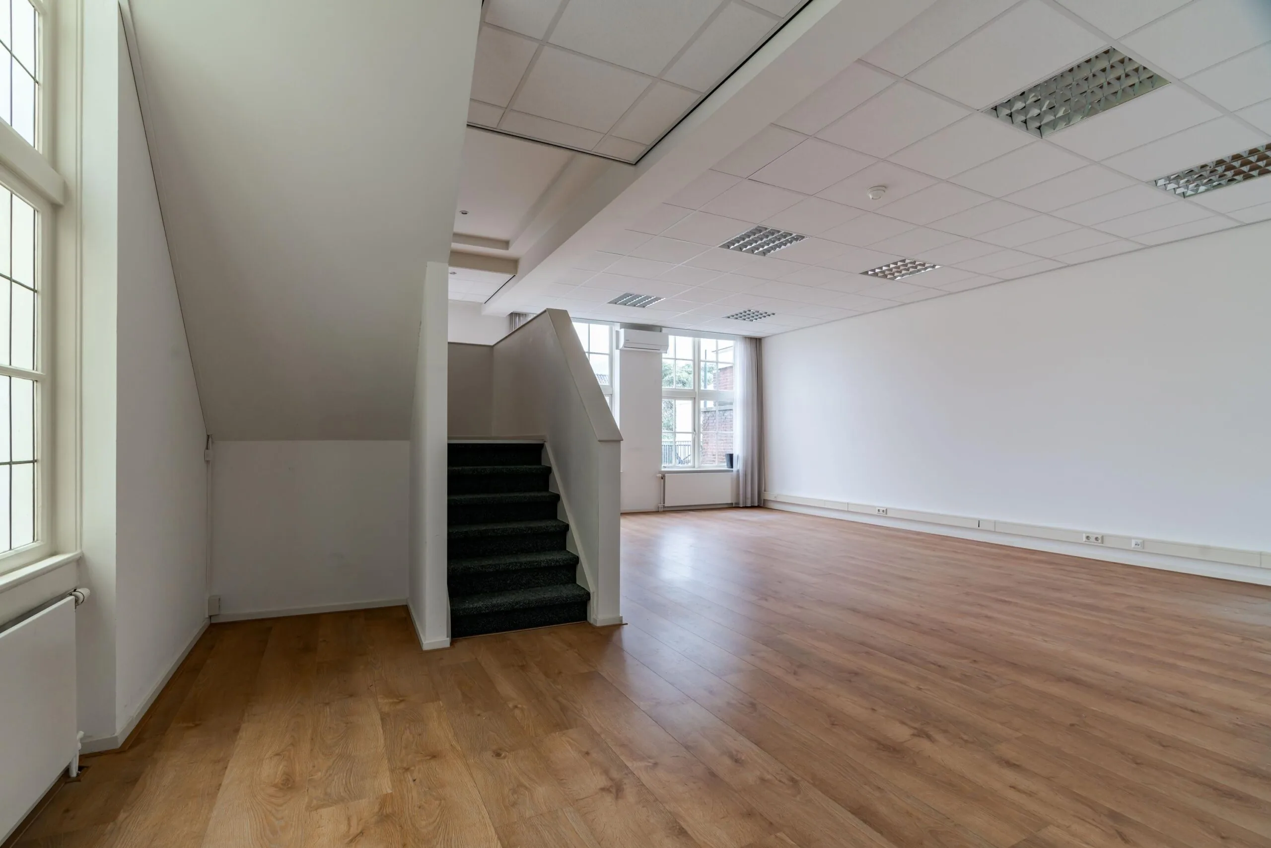 Licht en ruim interieur met houten vloer, witte muren, systeemplafond en een trap in een pand aan het Lange Voorhout.