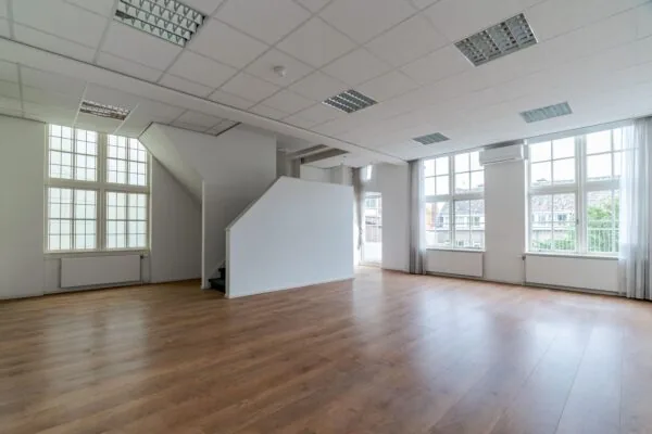 Licht en ruim kantoor of woonruimte aan het Lange Voorhout met grote ramen, houten vloer en een open trap.