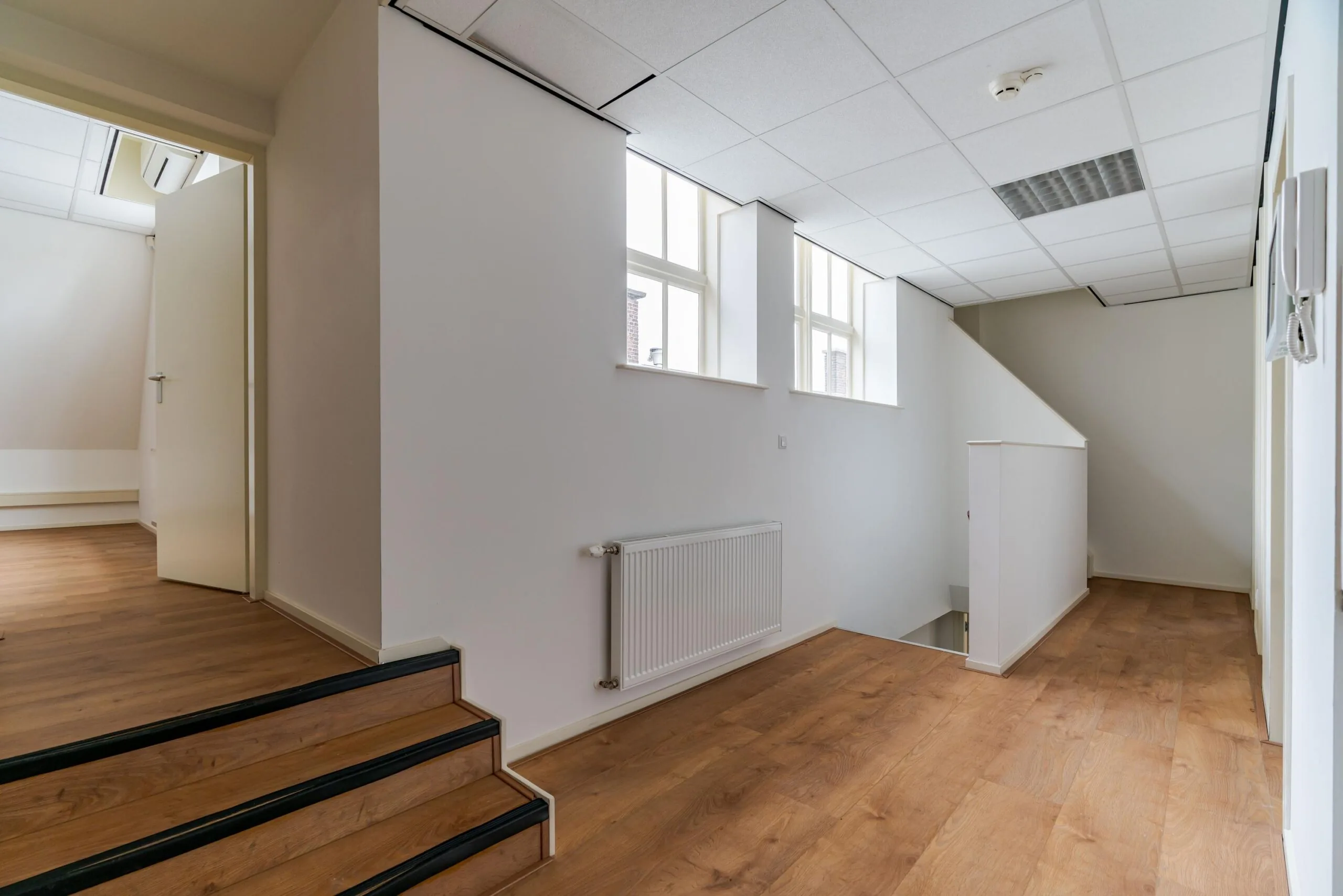 Lichtovergoten overloop met houten vloer, witte muren en trap in een pand aan het Lange Voorhout.
