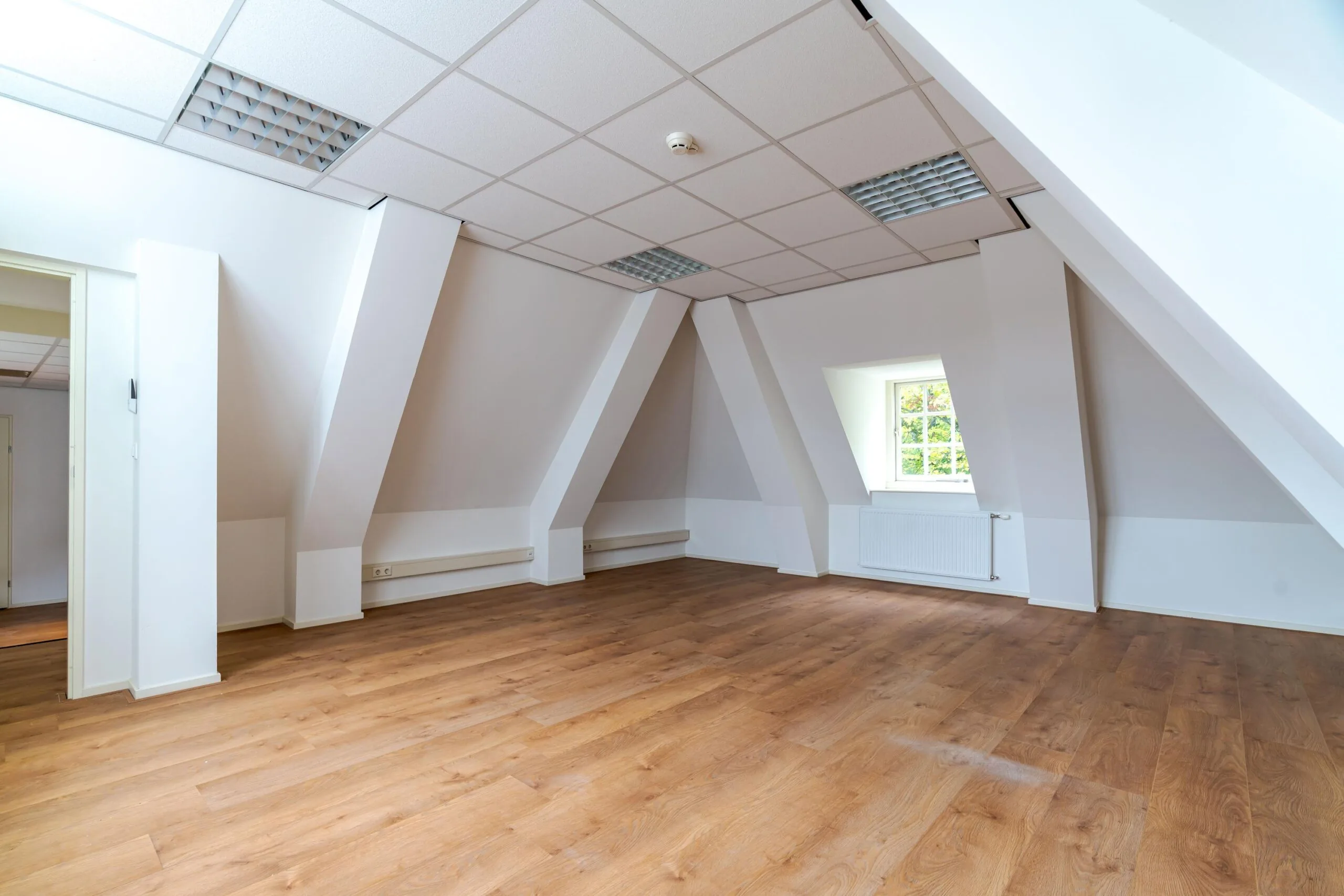 Licht en ruim zolderkantoor met houten vloer, schuin dak en een raam aan de Lange Voorhout.