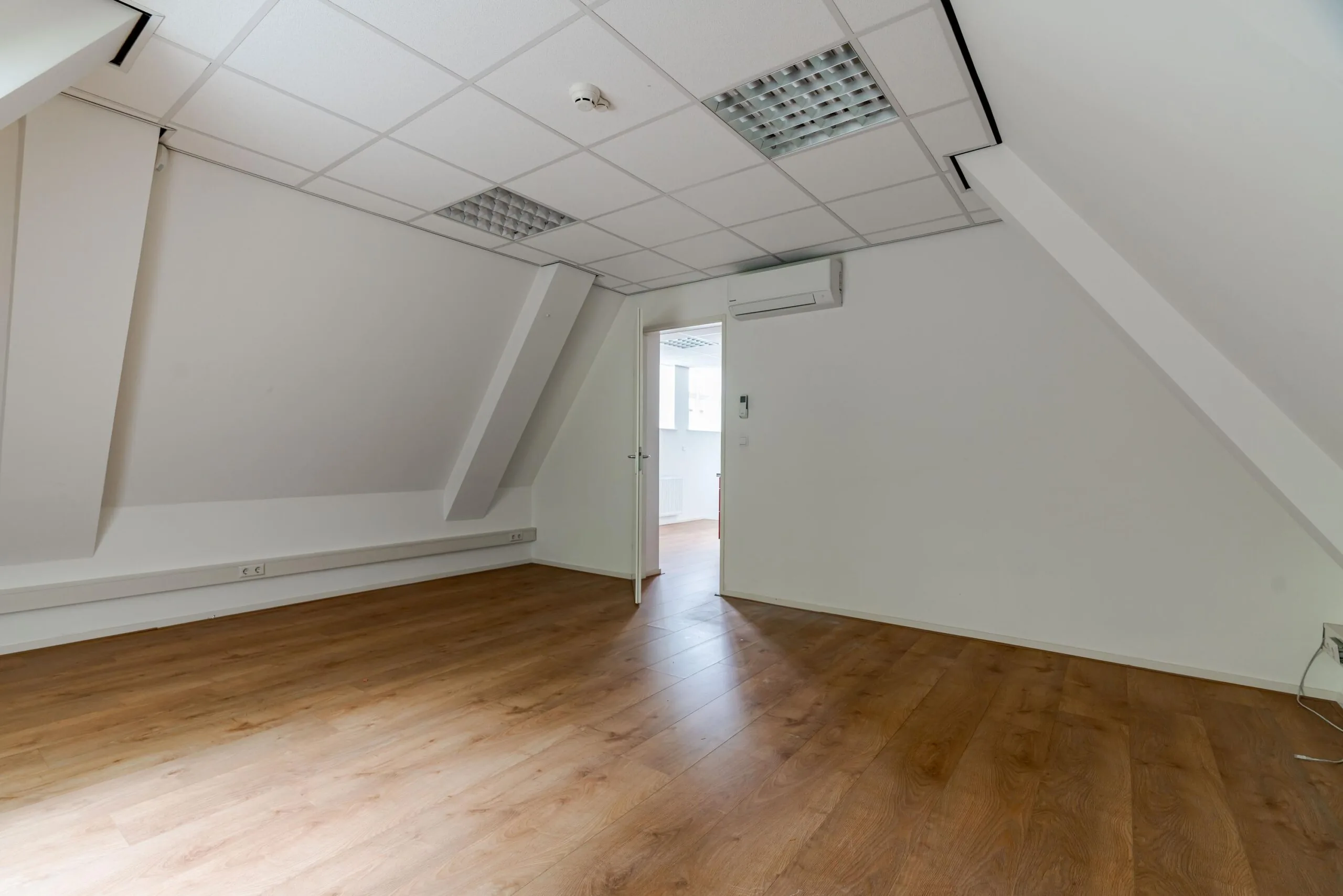 Lege kantoorruimte met schuin dak, systeemplafond en houten vloer aan het Lange Voorhout.