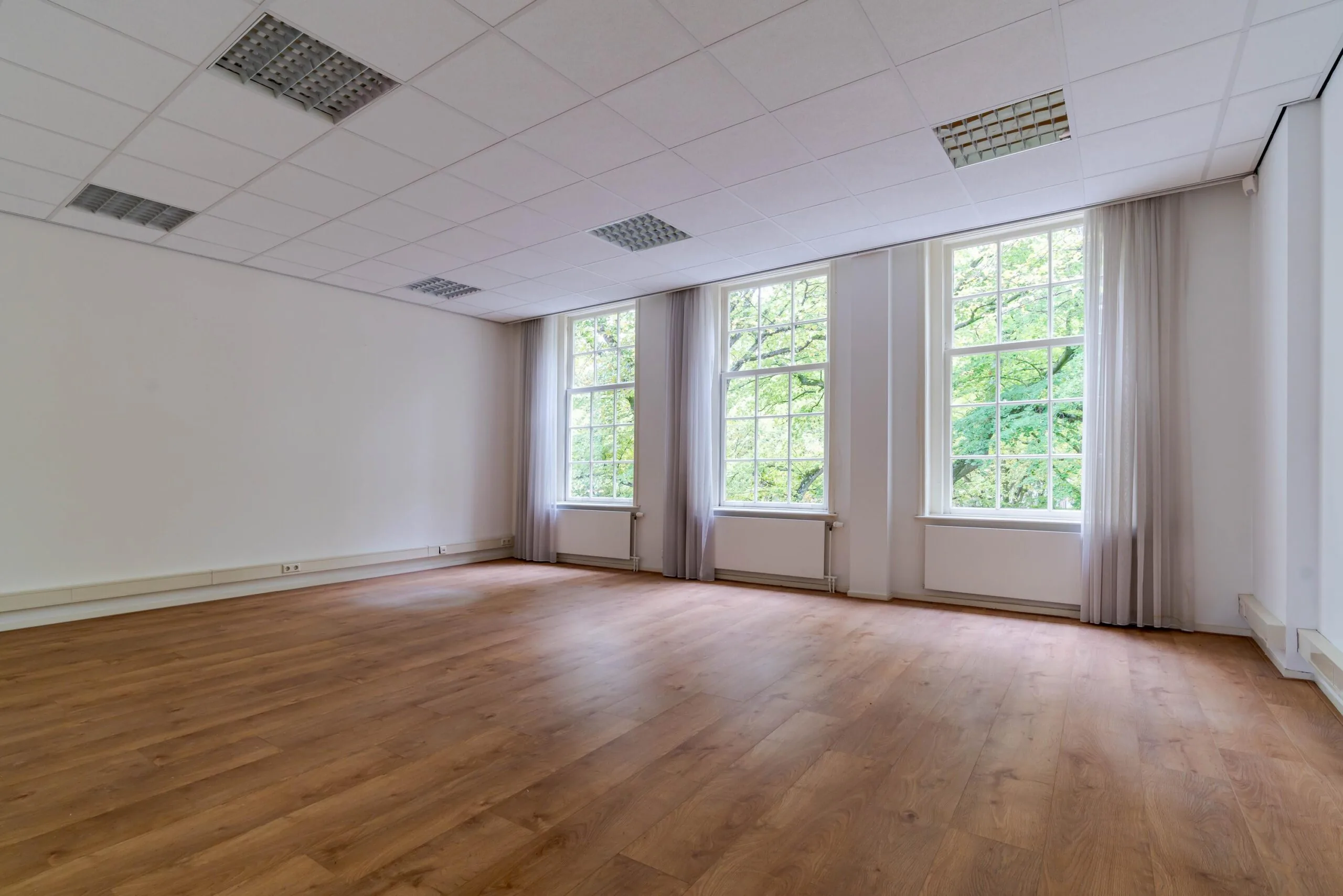 Licht en ruim leeg kantoor met houten vloer en grote ramen aan het Lange Voorhout.