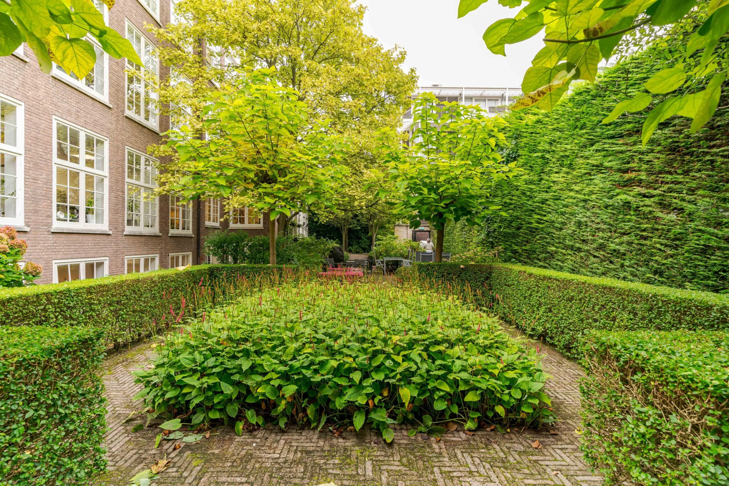 Verzorgde binnentuin aan het Lange Voorhout met heggen, bloemperken en bomen omringd door gebouwen.