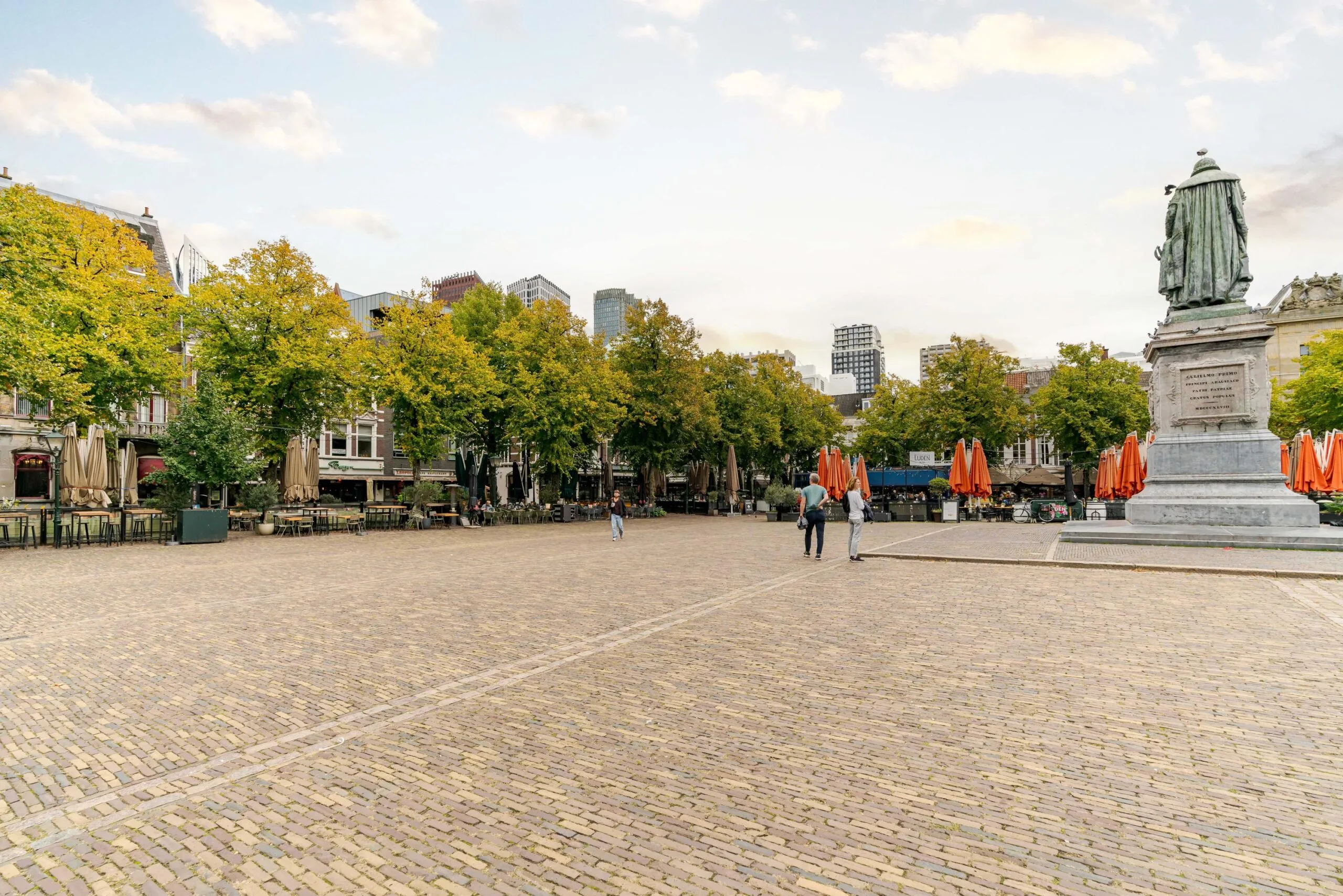 Plein met terrasjes, bomen en het standbeeld van Johan de Witt aan het Lange Voorhout in Den Haag.