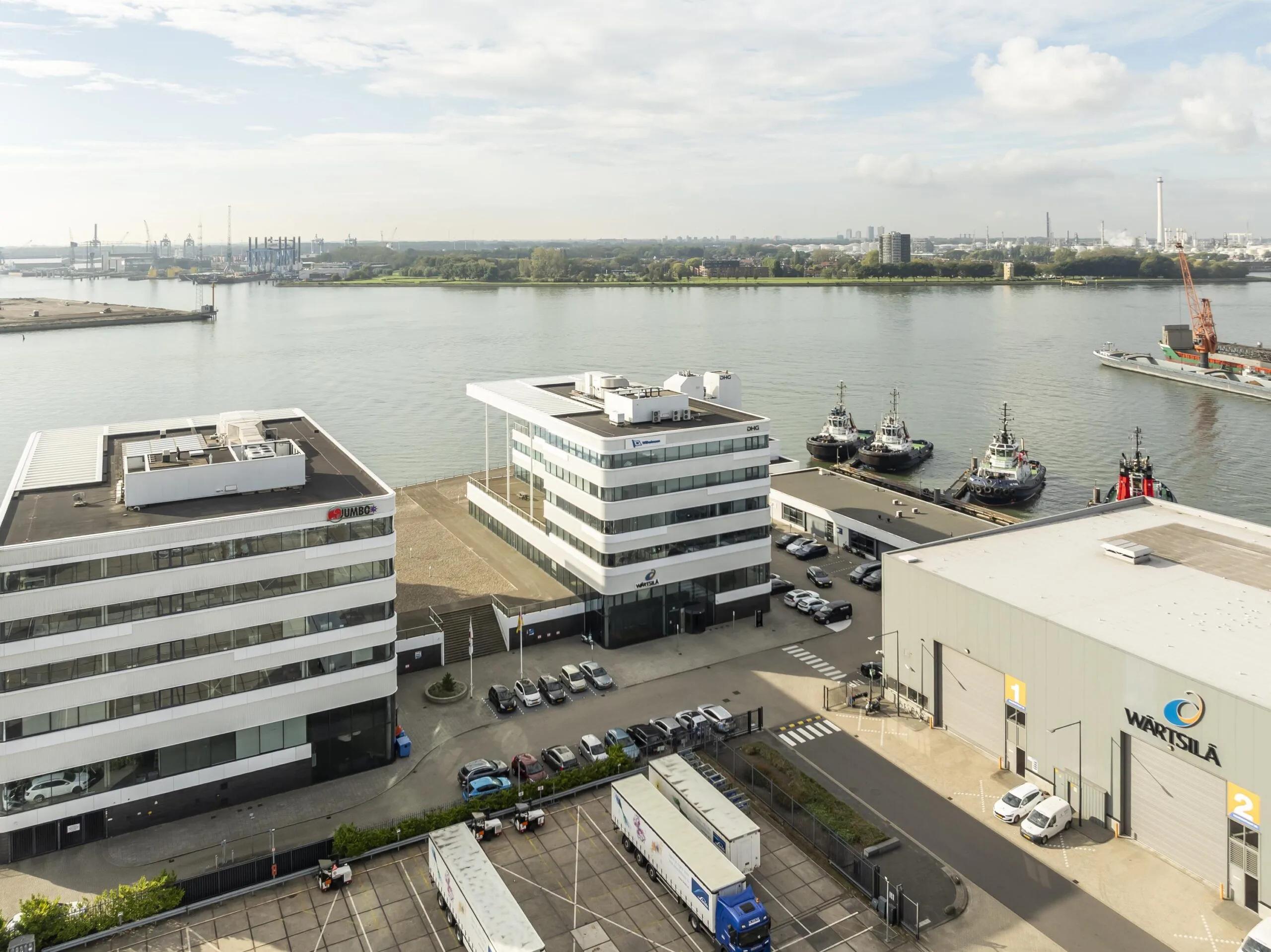 Luchtfoto van kantoorgebouwen en havenactiviteiten aan de Havenstraat met zicht op de rivier en meerdere afgemeerde sleepboten.