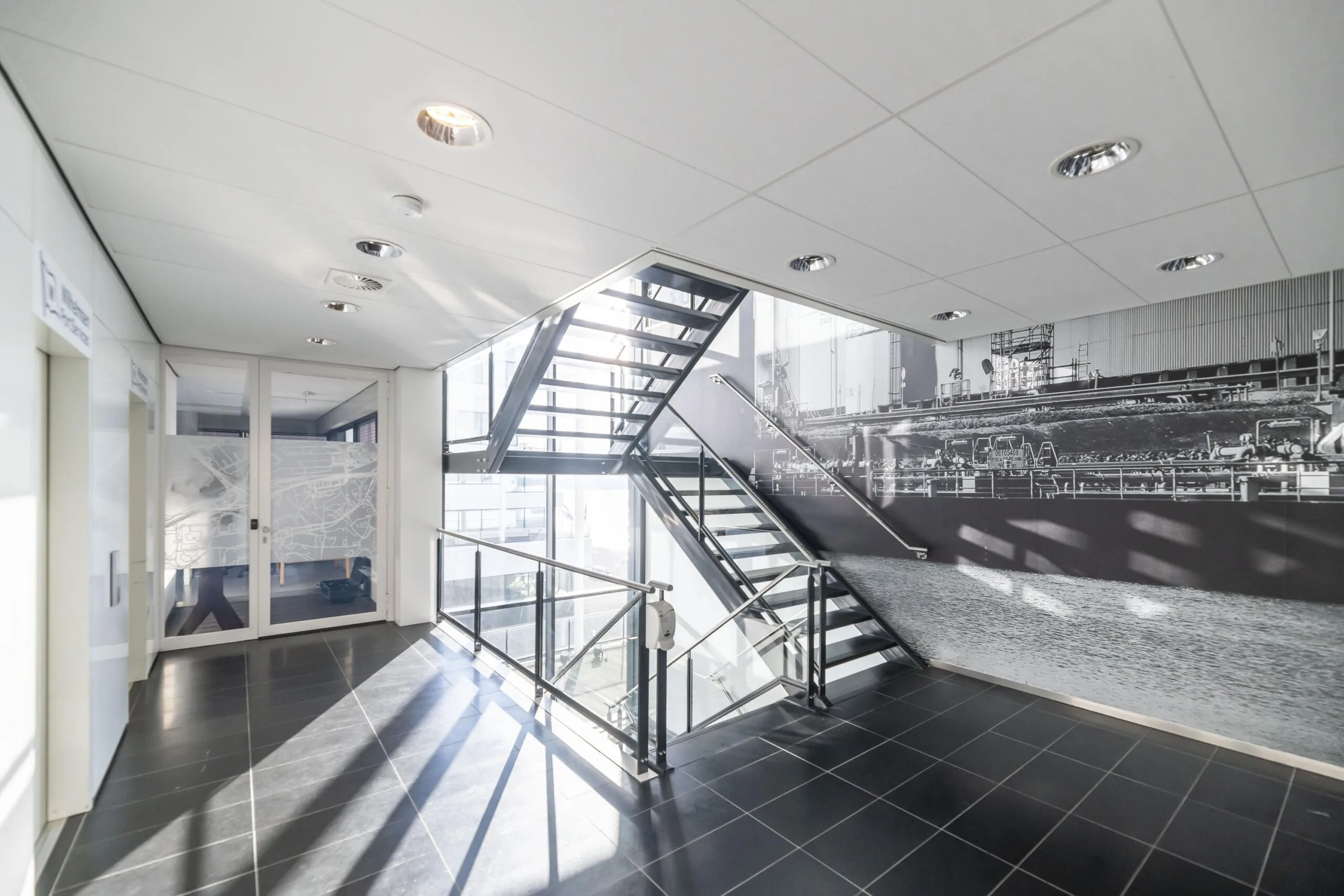 Moderne, lichte trappenhal met zwart-witte wandfoto van een industriële haven aan de Havenstraat.