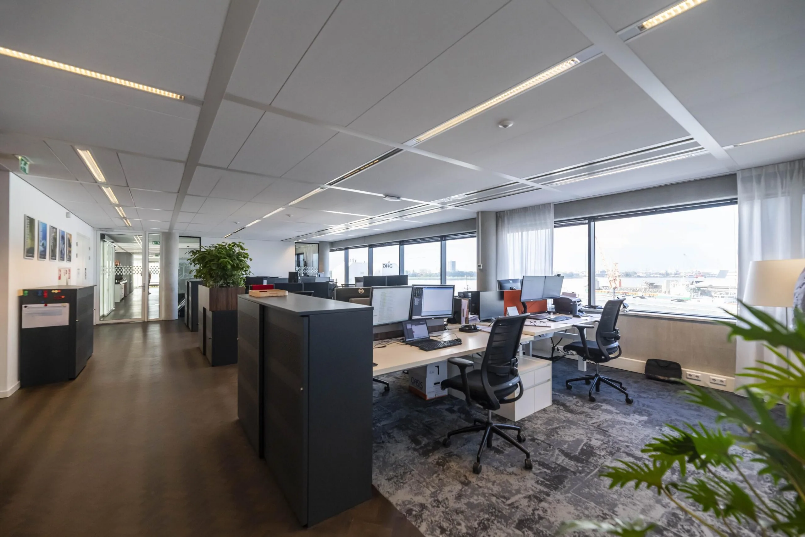 Modern kantoorinterieur aan de Havenstraat met bureaus, computers en uitzicht op een industriële haven.