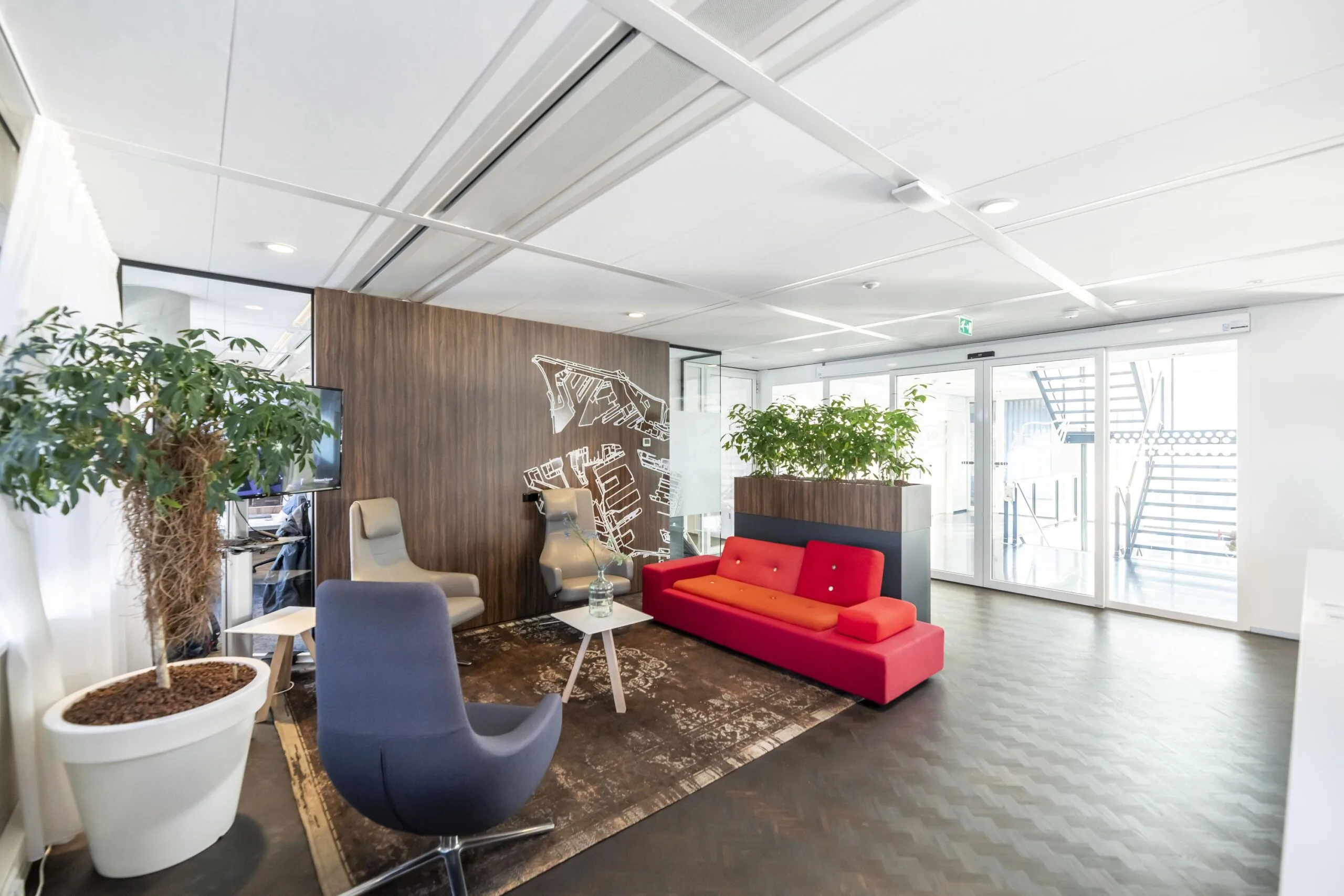 Moderne wachtruimte met kleurrijke zitmeubels, houten wanddecoratie en grote planten aan de Havenstraat.