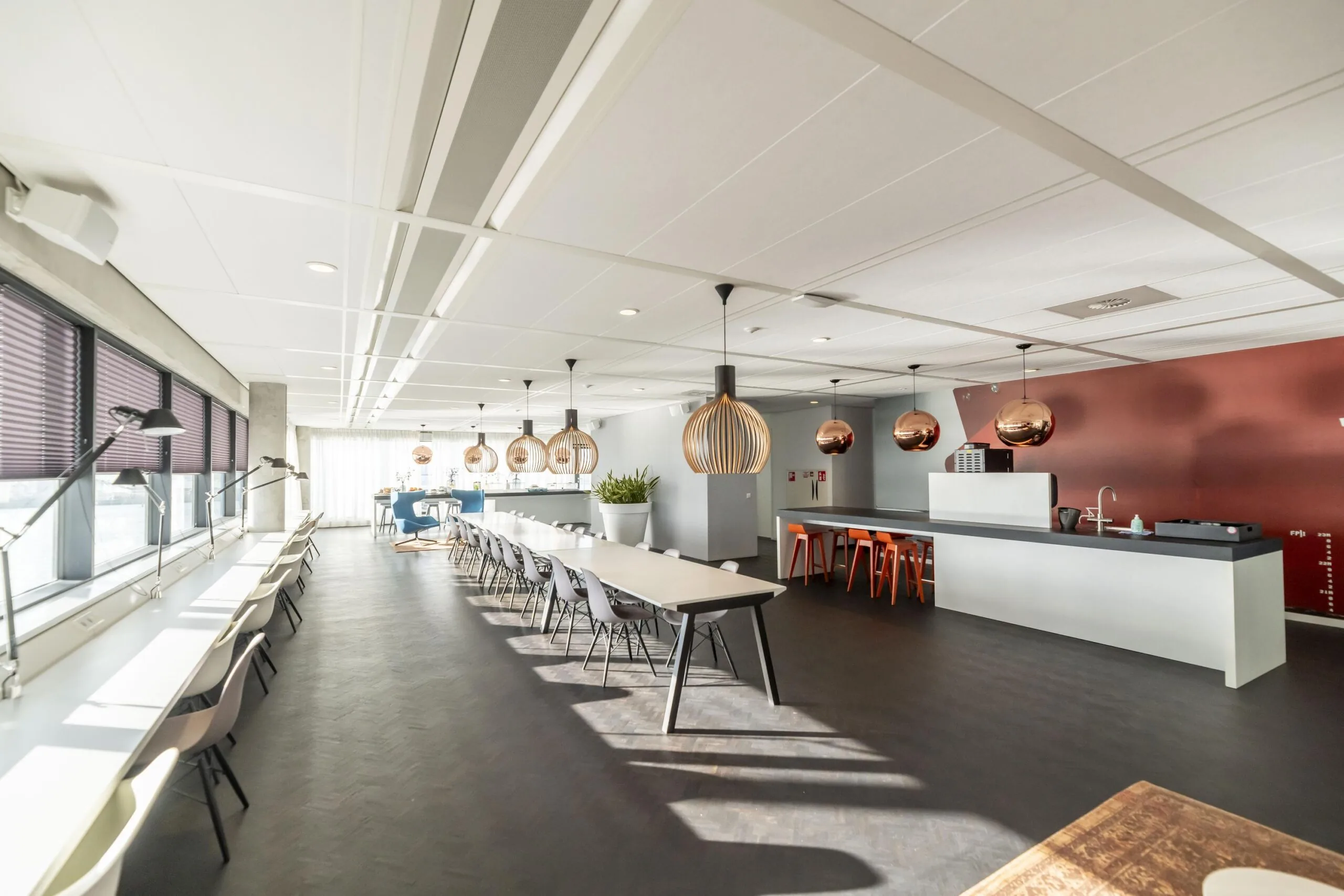 Moderne, lichte kantine aan de Havenstraat met lange tafels, designverlichting en een open keuken.
