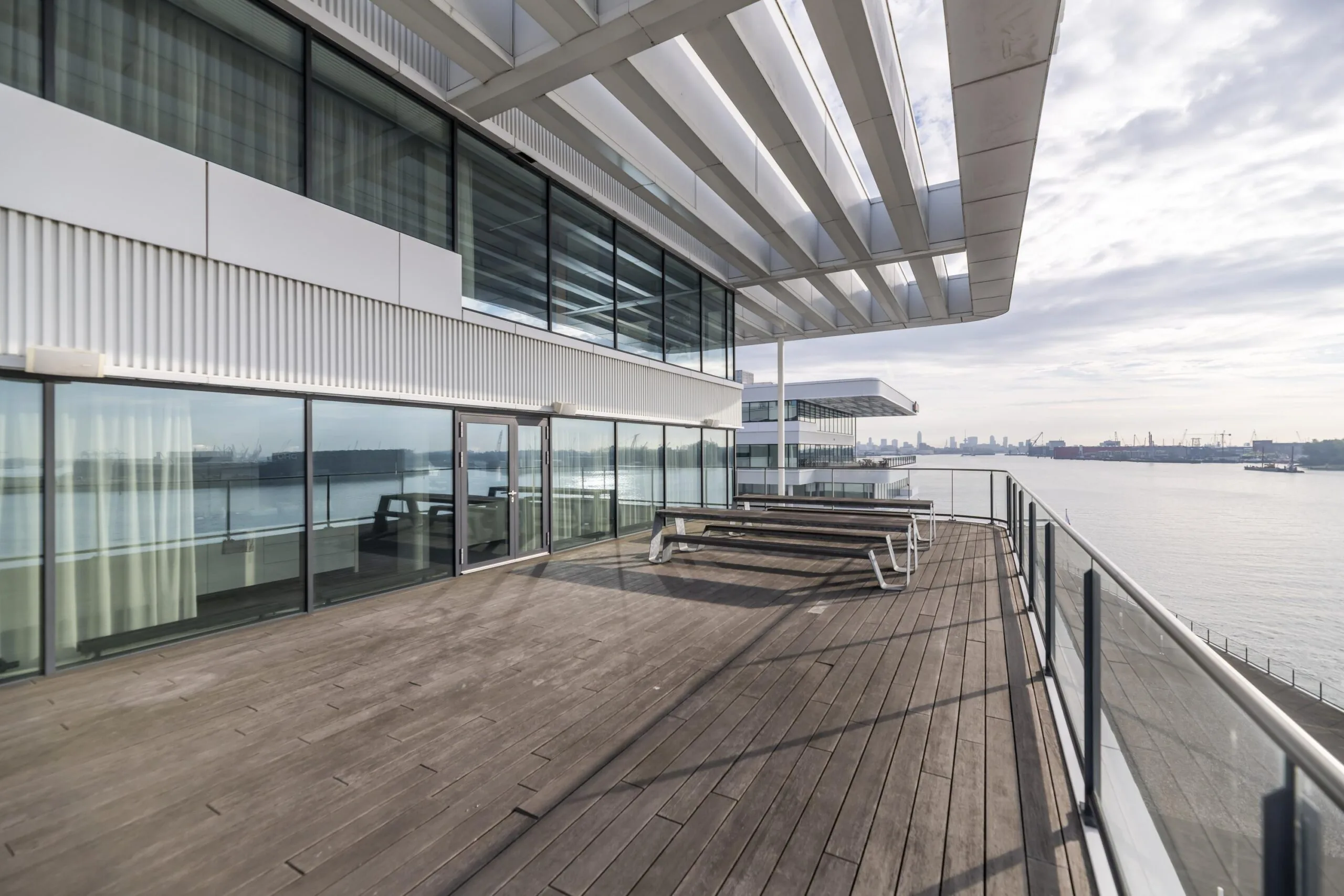 Houten dakterras met zitbanken aan het water bij een modern kantoorpand aan de Havenstraat.