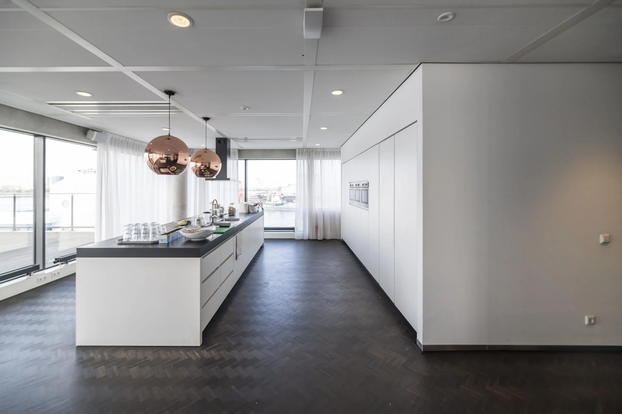 Moderne, lichte keuken aan de Havenstraat met kookeiland, koperkleurige hanglampen en uitzicht op het water.