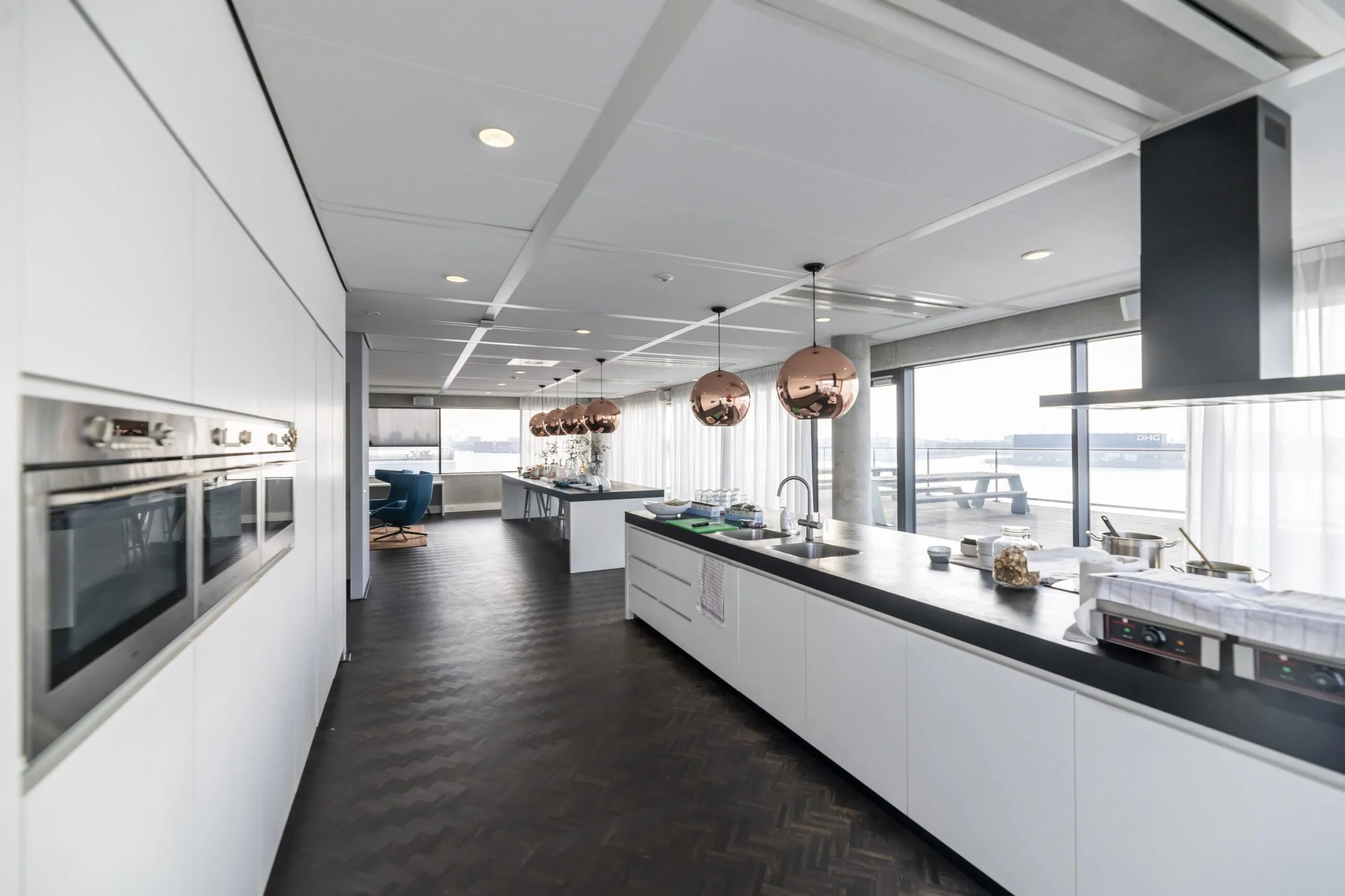 Moderne open keuken aan de Havenstraat met witte kasten, zwarte vloer, koperen hanglampen en uitzicht op het water.