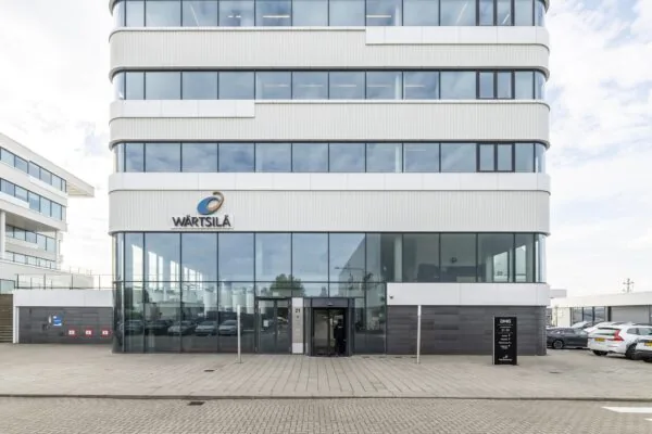 Vooraanzicht van het moderne kantoorpand van Wärtsilä aan de Havenstraat, met glazen entree en geparkeerde auto's ervoor.
