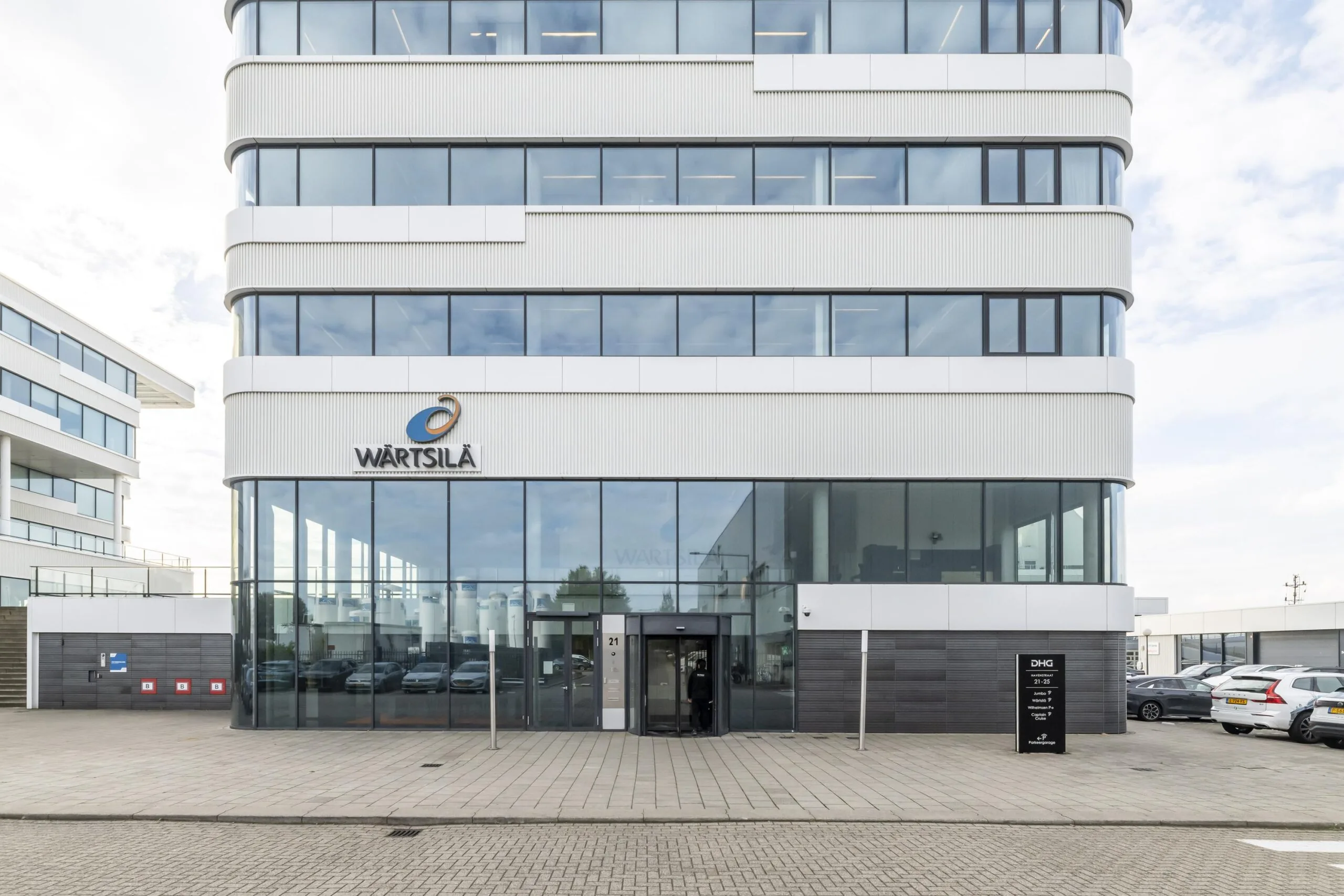 Vooraanzicht van het moderne kantoorpand van Wärtsilä aan de Havenstraat, met glazen entree en geparkeerde auto's ervoor.