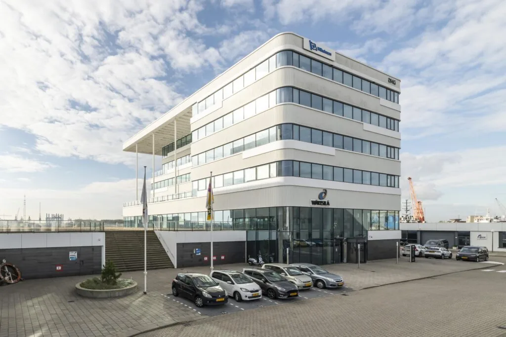Modern kantoorgebouw aan de Havenstraat met logo's van Wärtsilä, DMC en Winel op de gevel en geparkeerde auto's op de voorgrond.
