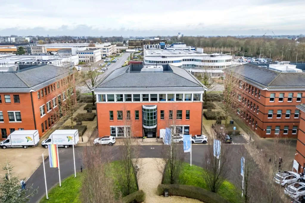 Luchtfoto van een modern kantoorgebouw aan de Lange Dreef, omringd door vergelijkbare rode bakstenen panden en geparkeerde voertuigen.