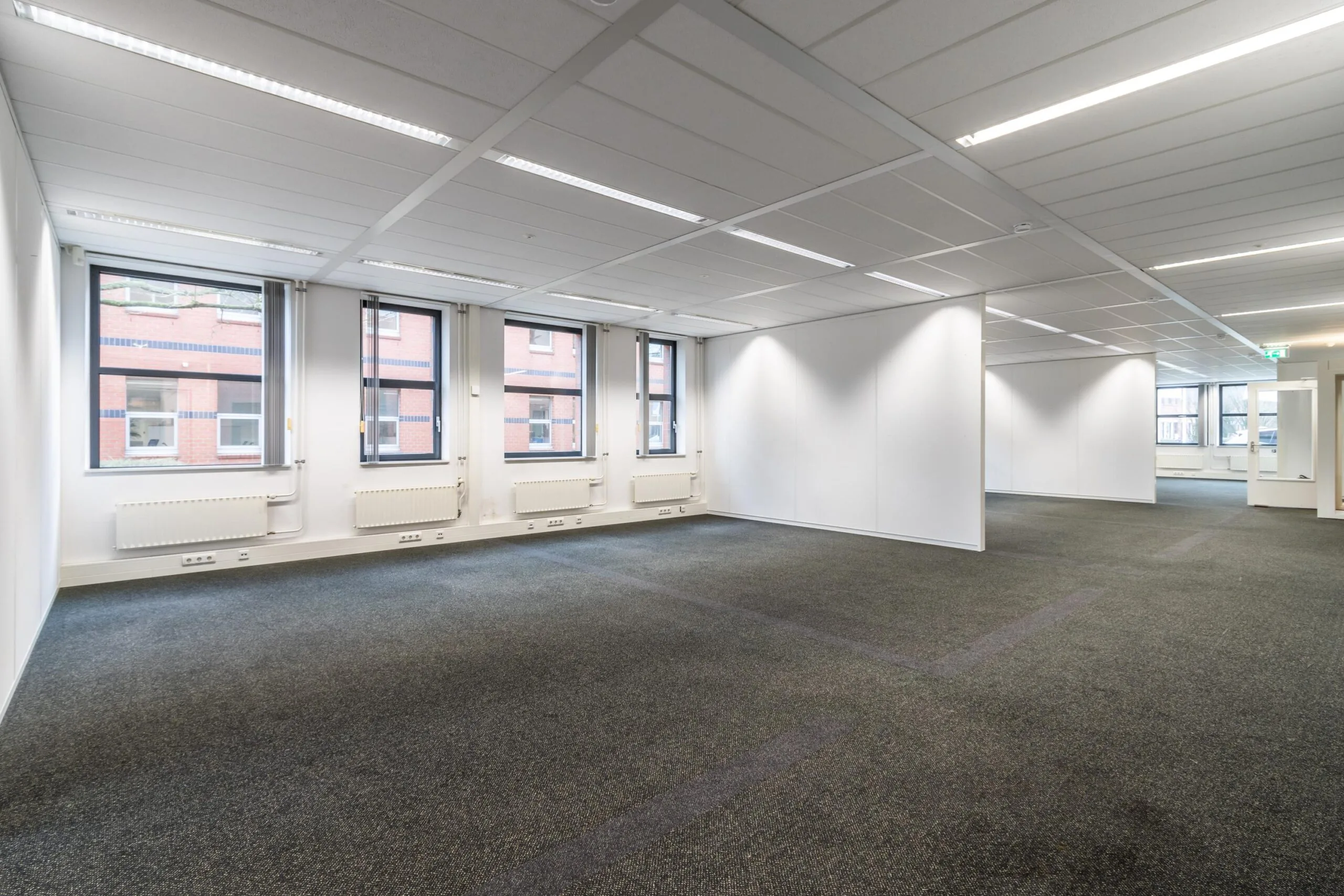 Leeg kantoorpand aan de Lange Dreef met grijze vloerbedekking, witte wanden en meerdere ramen.