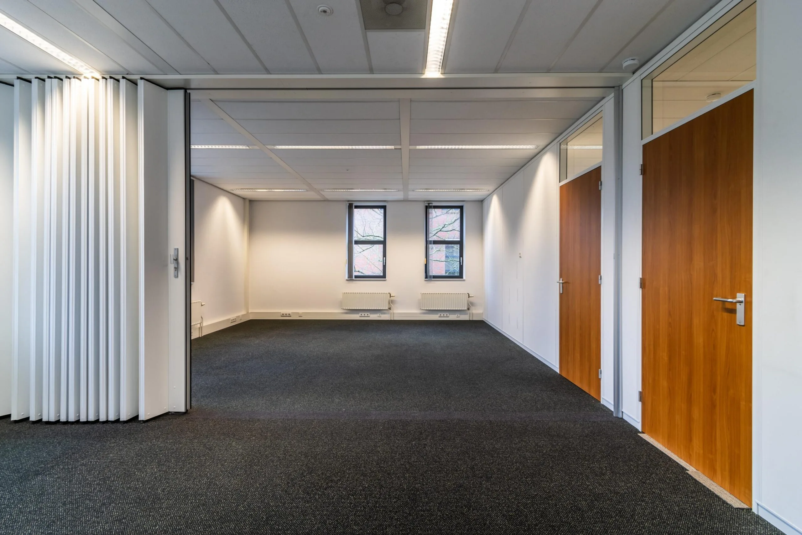 Lege kantoorruimte aan de Lange Dreef met twee ramen, systeemplafond en houten deuren.
