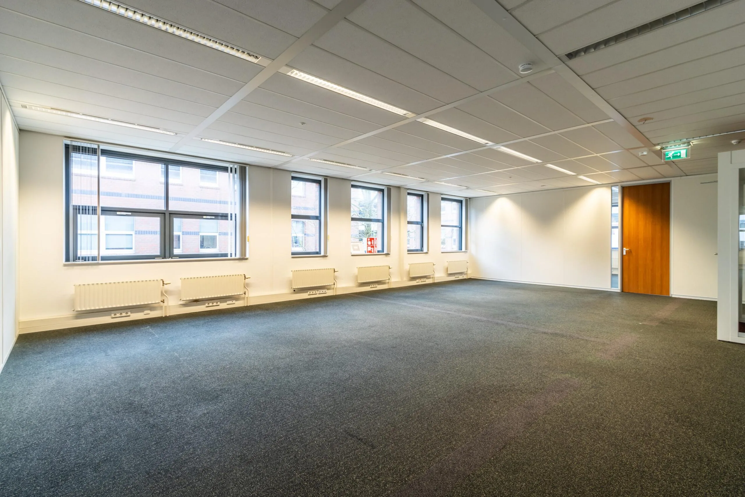 Licht en leeg kantoor aan de Lange Dreef met meerdere ramen, systeemplafond en grijs tapijt.