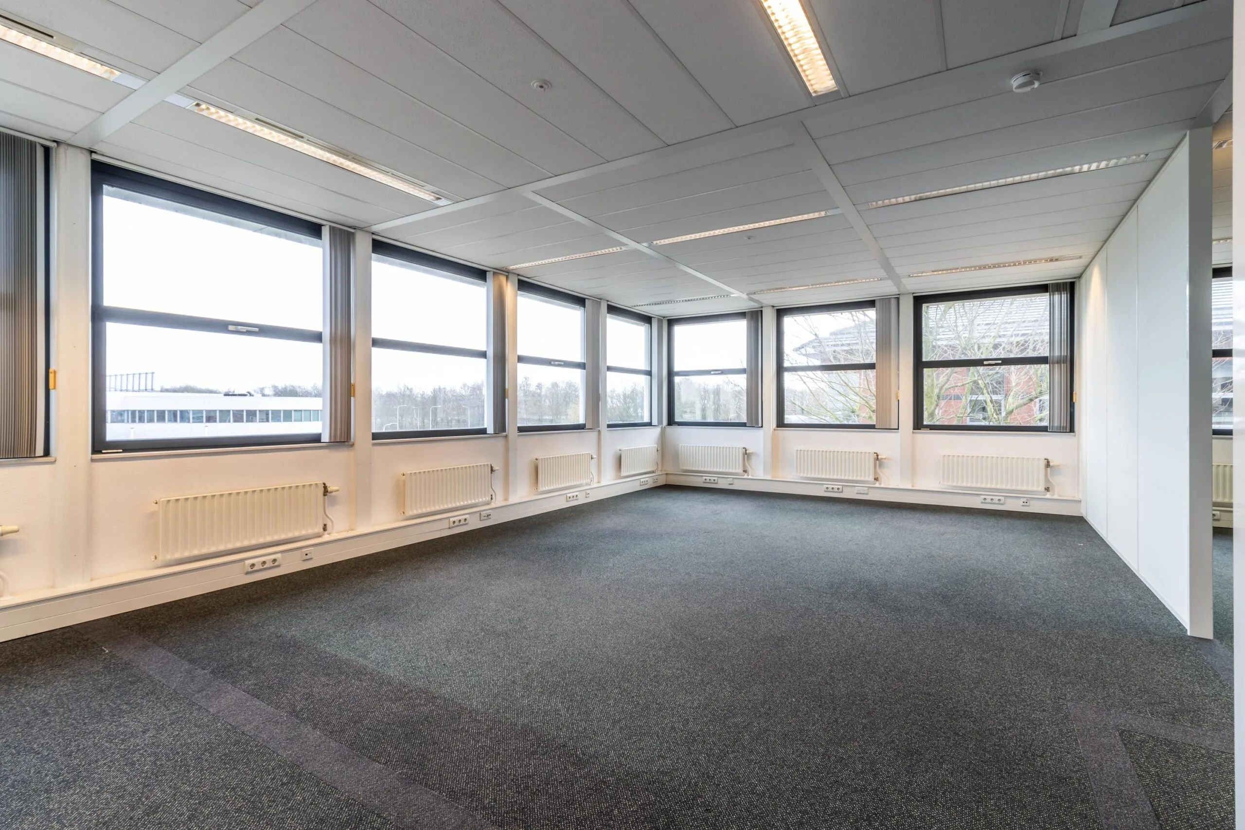 Licht, leeg kantoor met tapijtvloer en grote ramen aan de Lange Dreef.