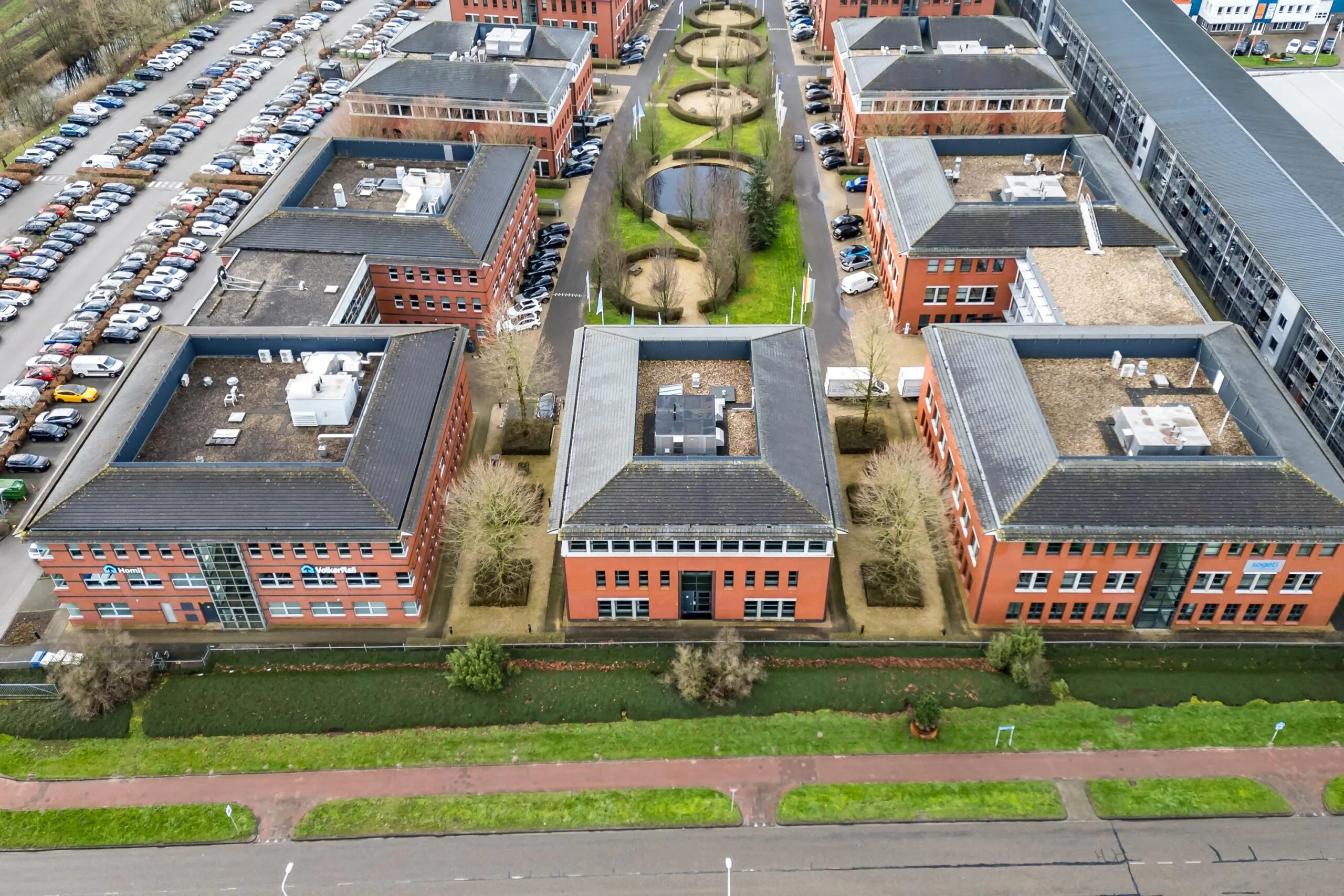 Luchtfoto van rode kantoorgebouwen aan de Lange Dreef met parkeerterreinen en een vijver in het midden.