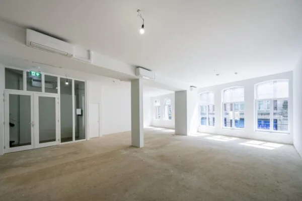 Licht en leeg commercieel interieur aan het Damrak met grote ramen en witte muren.