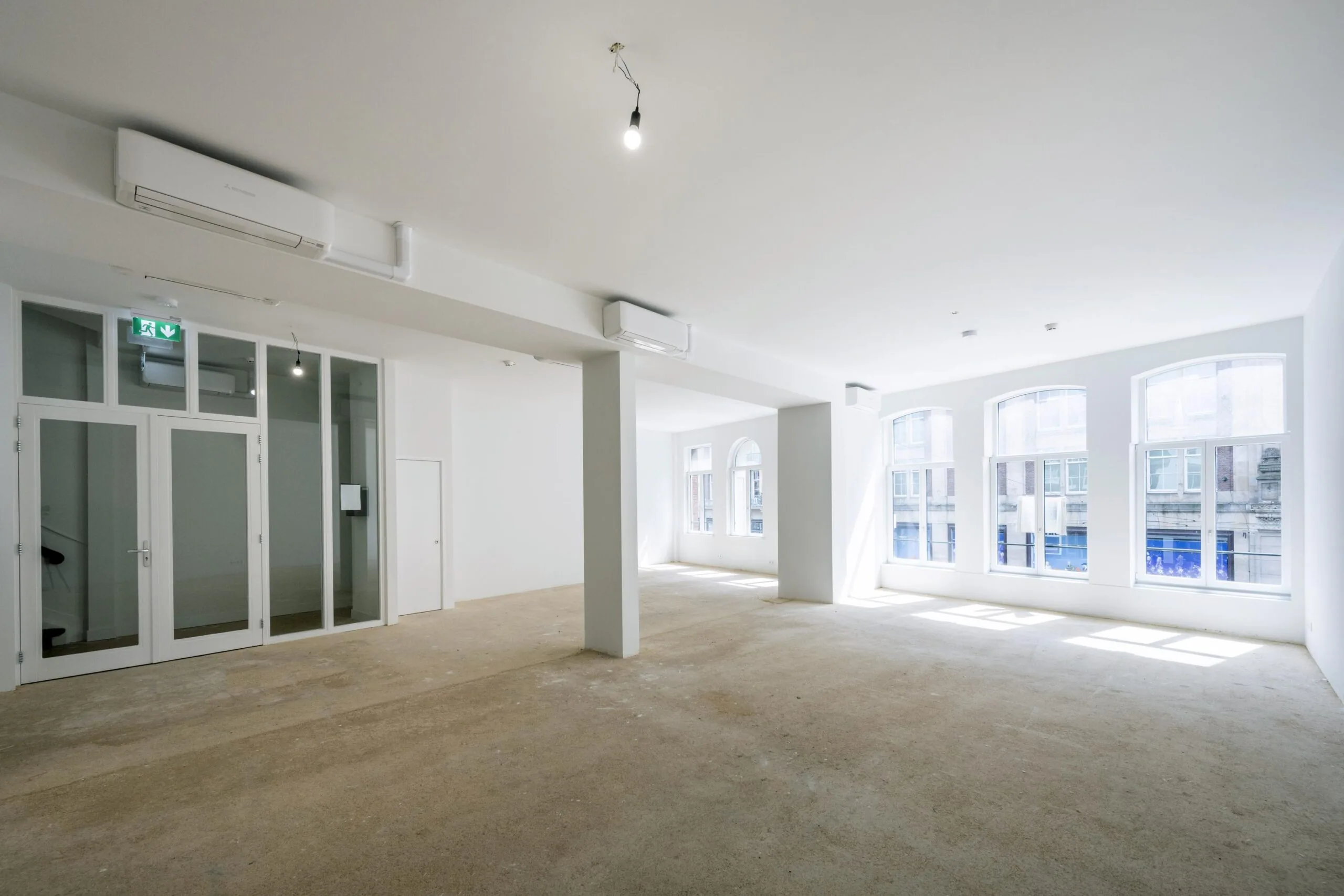 Licht en leeg commercieel interieur aan het Damrak met grote ramen en witte muren.