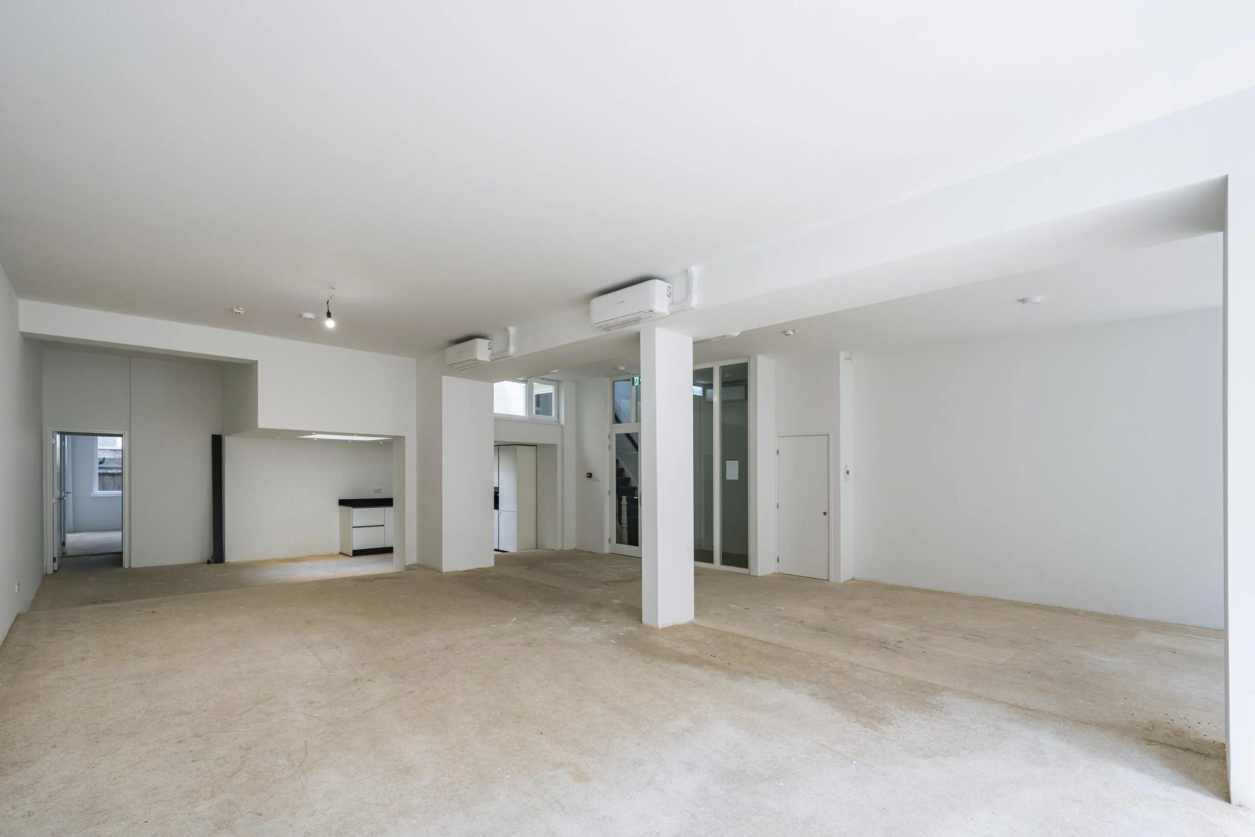 Ruime, lichte commerciële ruimte op de Damrak met witte muren, steunpilaren en open indeling.