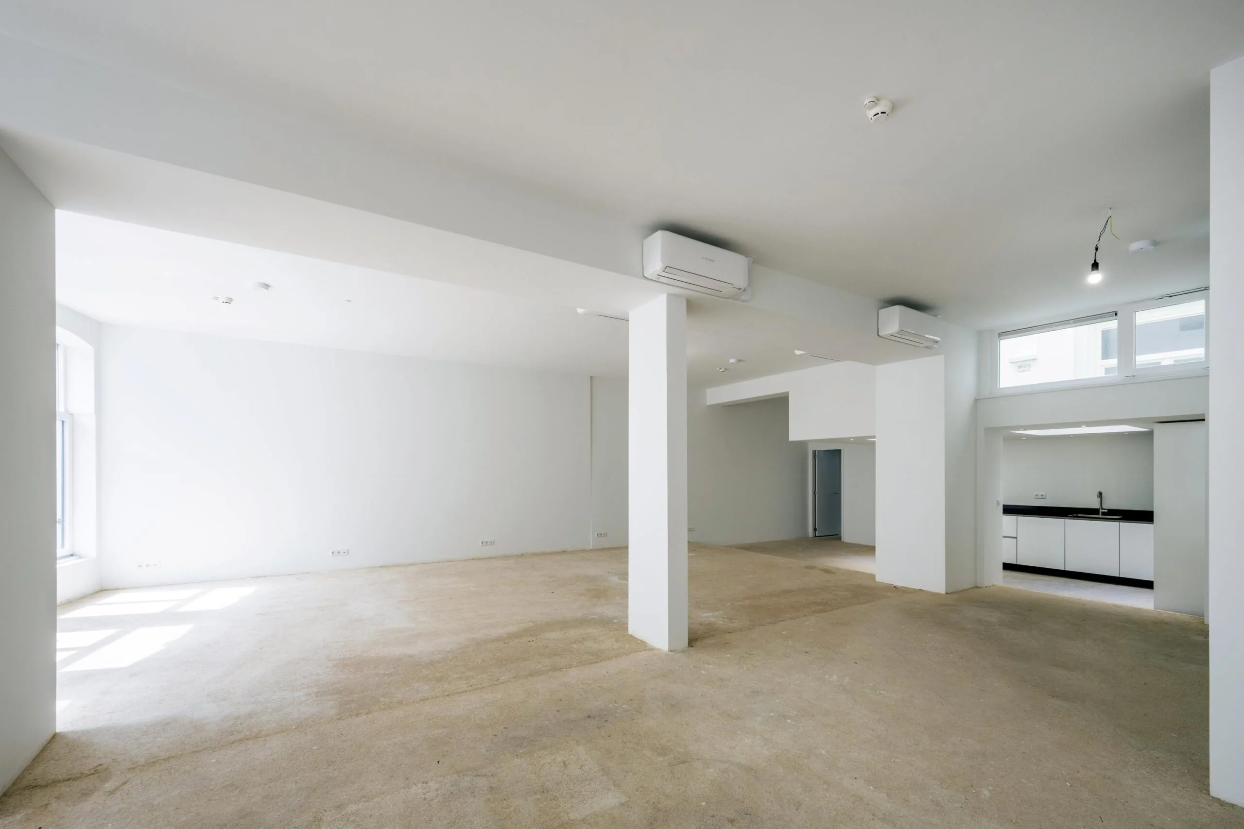 Lichte, lege bedrijfsruimte aan de Damrak met zicht op een open keuken en meerdere ramen.