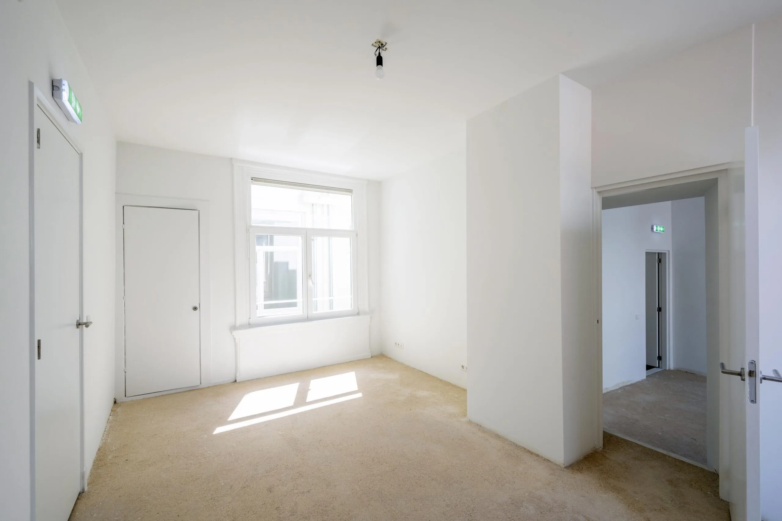 Lege, lichtinvalrijke kamer aan het Damrak met witte muren, deuren en kale vloer.