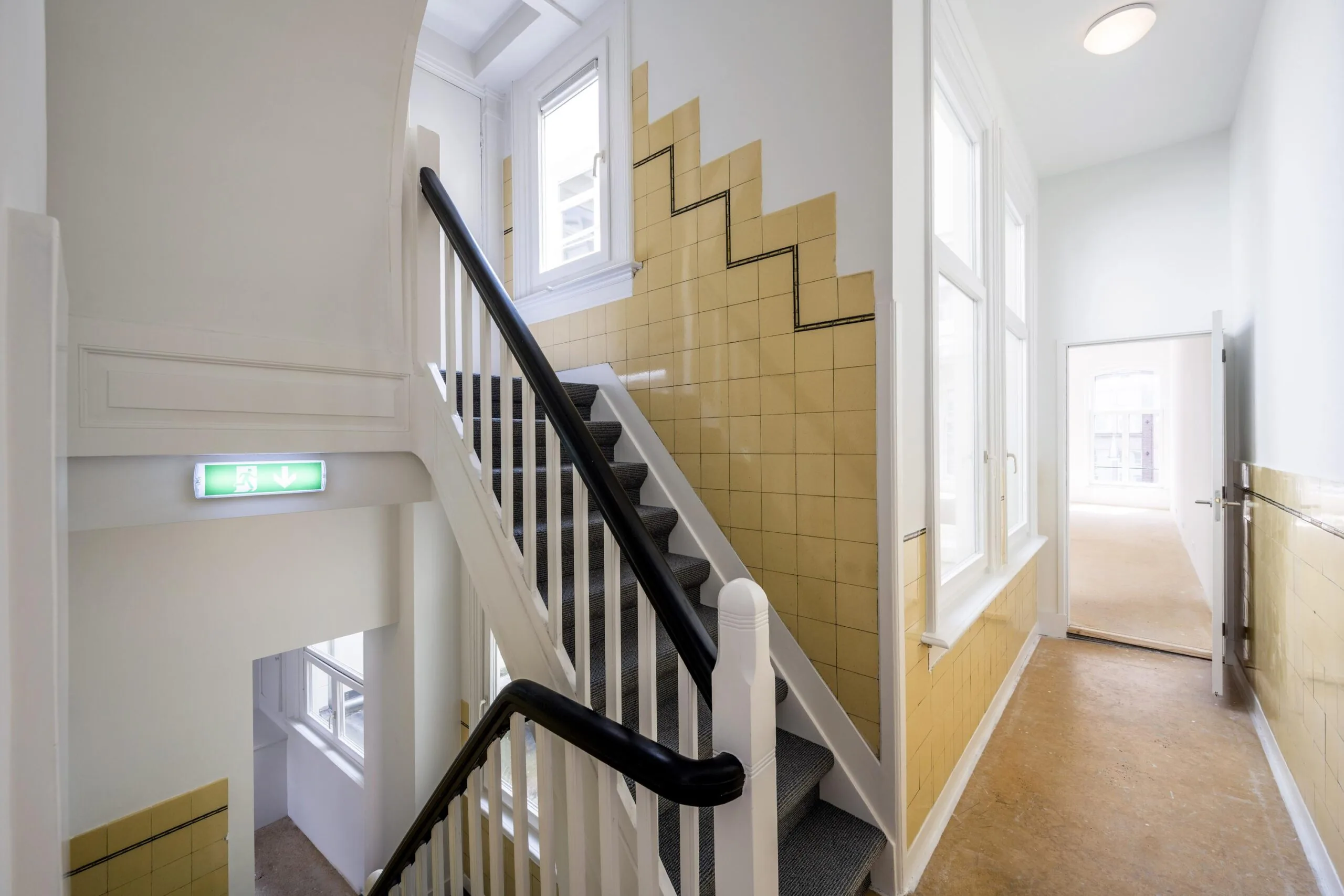 Trapportaal met gele wandtegels en zwarte leuning in een pand aan het Damrak.