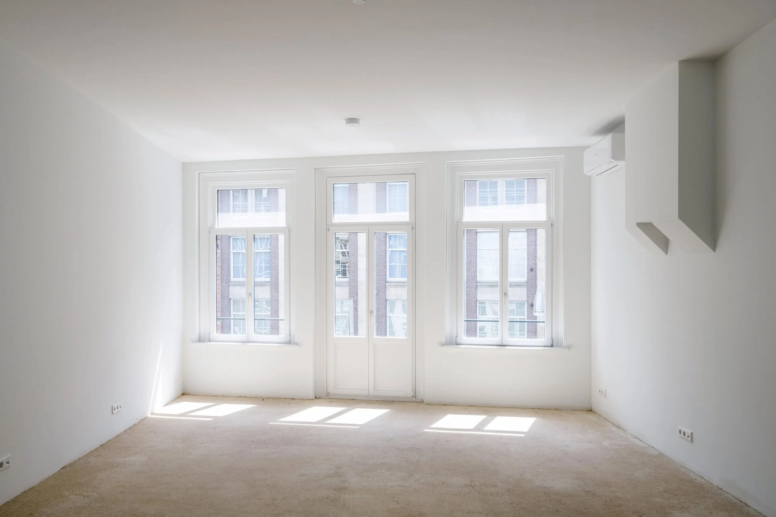 Licht en leeg appartement aan de Damrak met grote ramen en wit afgewerkte muren.