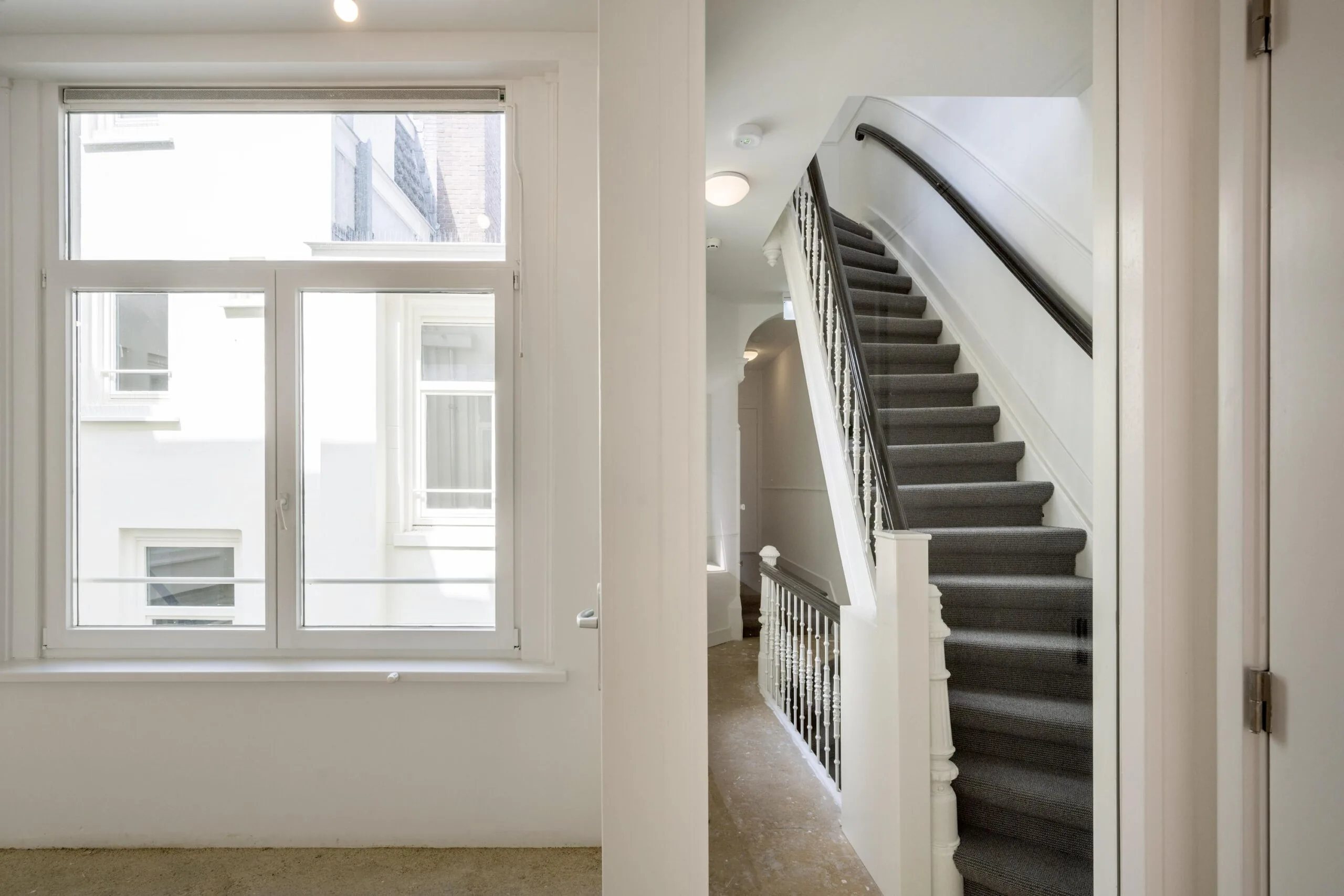 Trapopgang en raam in licht trappenhuis van woning aan het Damrak in Amsterdam.