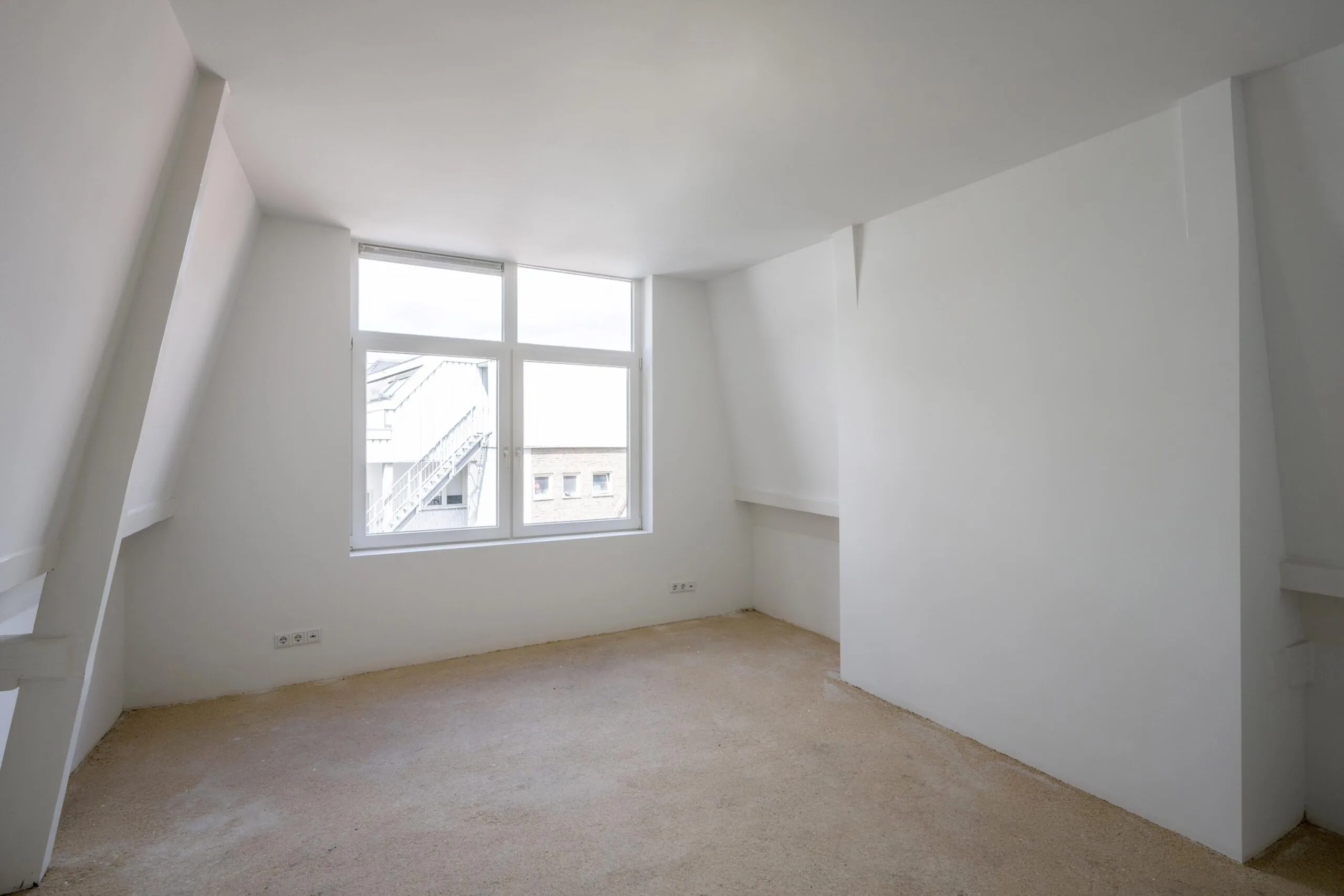 Lichte, lege zolderkamer aan het Damrak met schuin dak en groot raam.