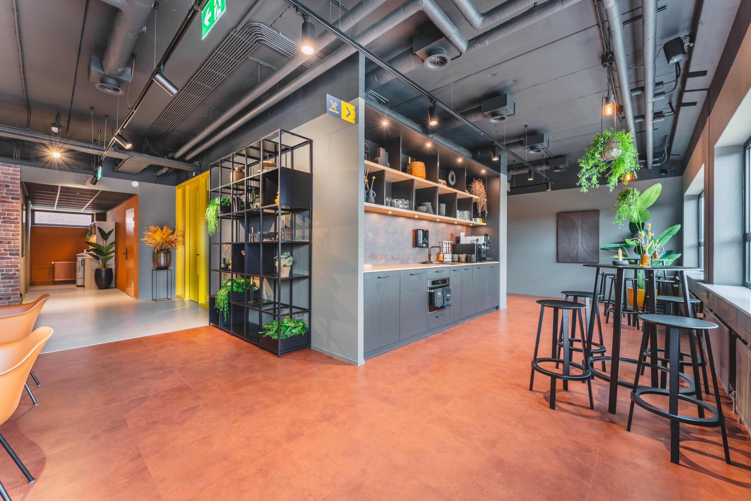 Een modern kantoorinterieur met een keukenhoek, eetgedeelte en veel groen.