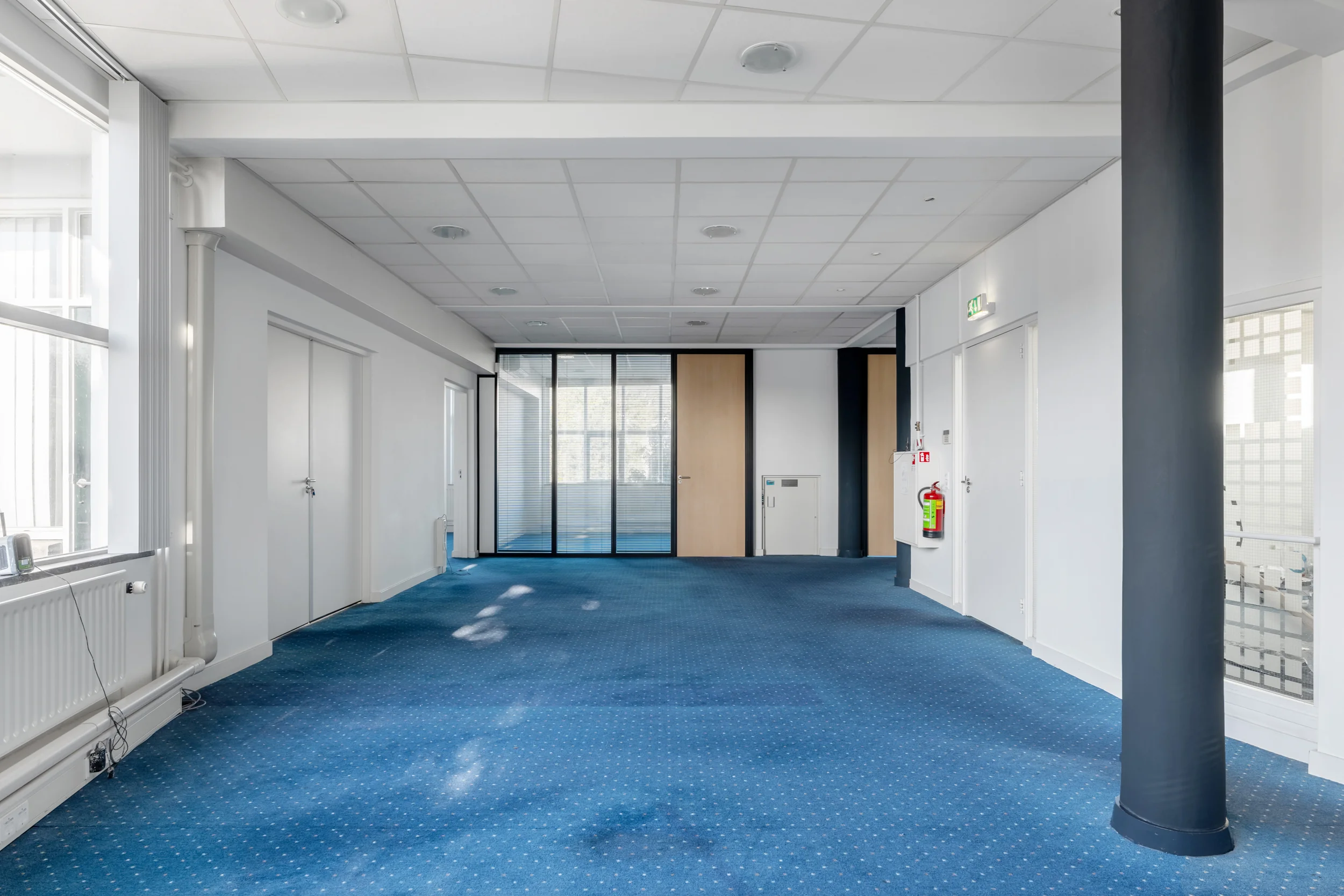 Bright hallway in an office building on Rozenlaan with blue carpet, white walls, and glass partition doors.