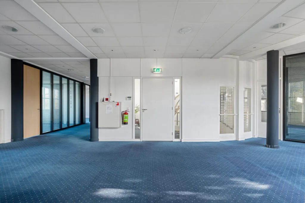 Modern office hallway with blue carpet, white walls, and glass-panel doors at Rozenlaan.