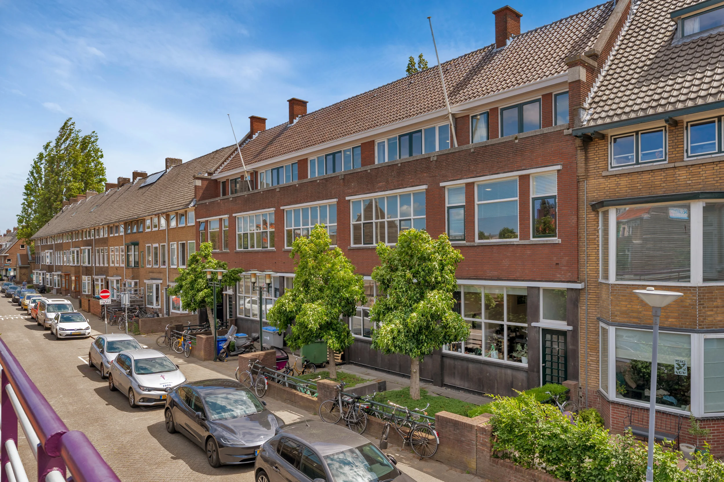 Street view of Rozenlaan showing a row of brick townhouses, parked cars, trees, and bicycles on a sunny day.