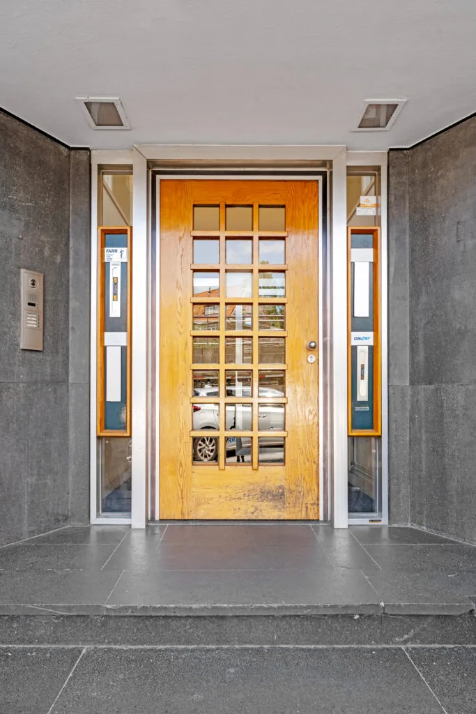 Entrance of an apartment building on Rozenlaan with a wooden door featuring square glass panels and intercom system.
