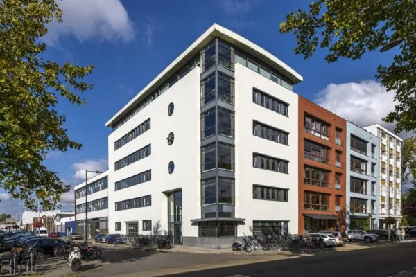 Modern apartment and office buildings on Helicopterstraat in a sunny urban street scene with parked cars and bicycles.