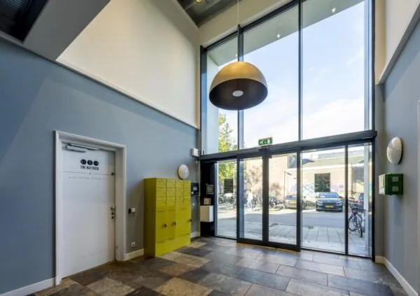 Modern entrance hall with large windows, yellow mailboxes, and a door labeled "The Hattrick" at Helicopterstraat.