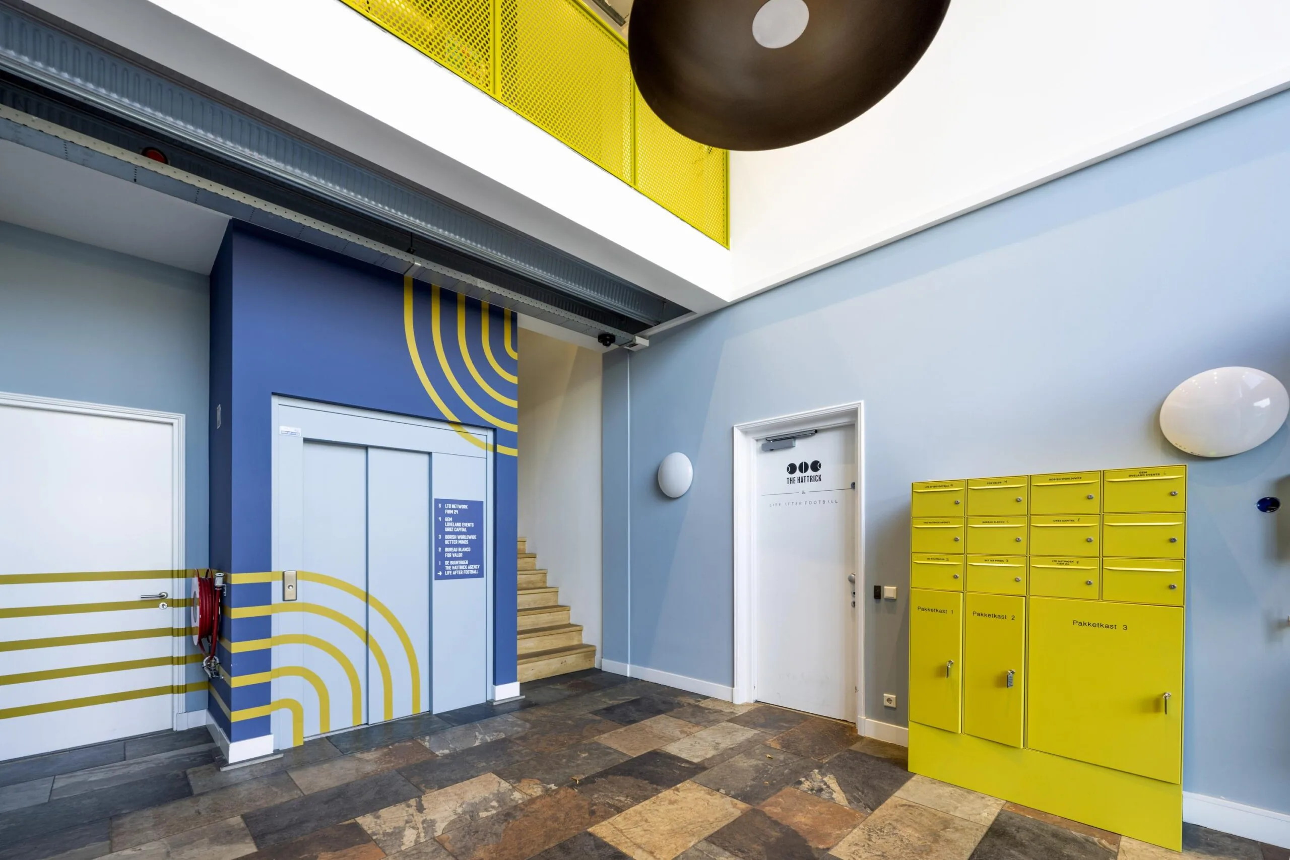 Modern apartment building lobby on Helicopterstraat with a blue elevator, yellow mail lockers, and staircase.