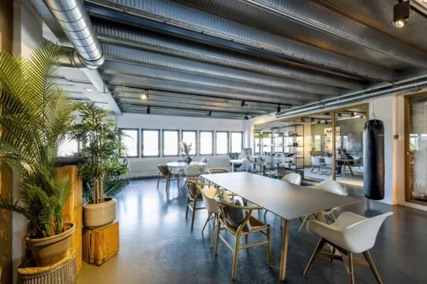Modern industrial-style office space on Helicopterstraat with large windows, contemporary furniture, indoor plants, and a punching bag.
