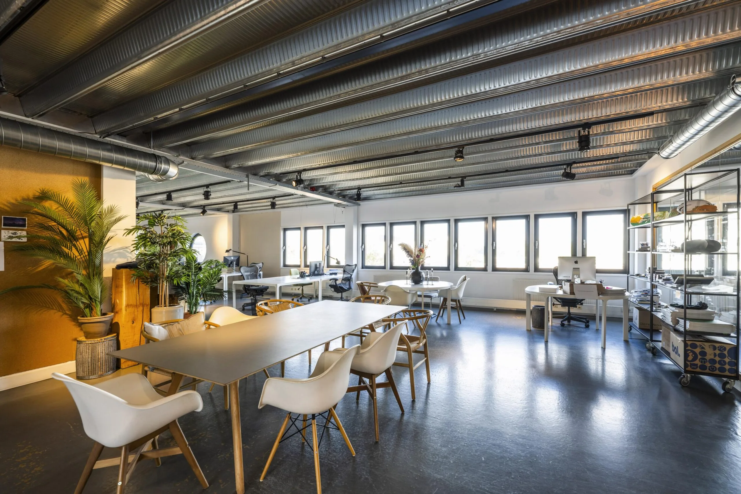 Modern open-plan office on Helicopterstraat with industrial ceiling, large windows, and mixed workspaces.