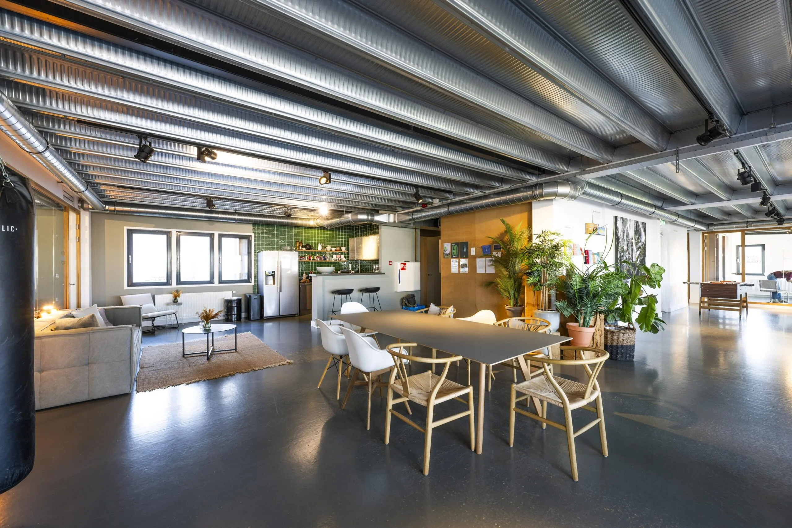 Modern industrial-style office lounge at Helicopterstraat with dining area, kitchen, seating, and indoor plants.