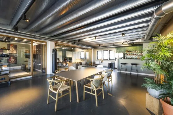 Modern industrial-style office interior with a meeting table, lounge area, bar, and glass-walled offices at Helicopterstraat.