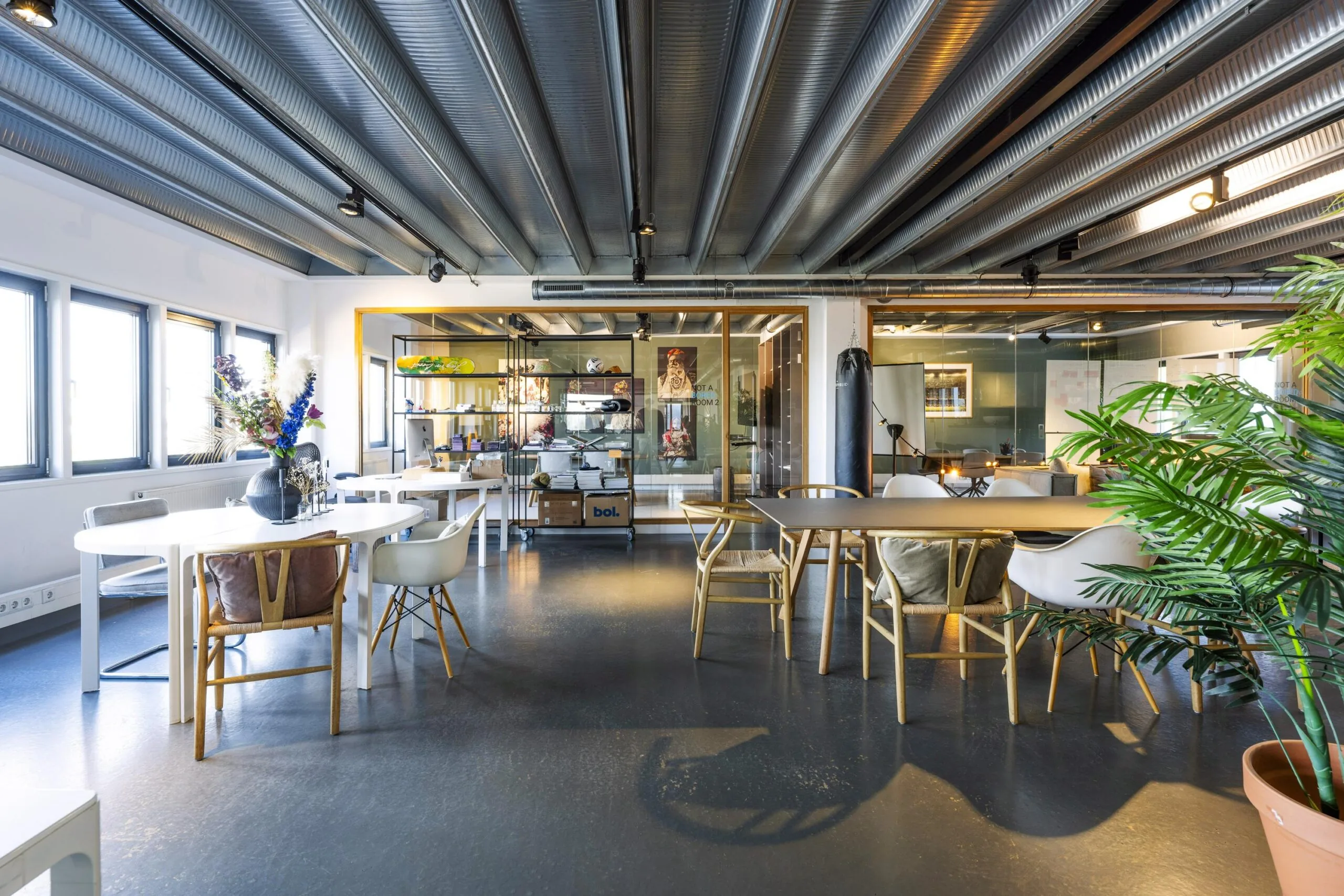 Modern industrial-style office space on Helicopterstraat with mixed seating areas, plants, and a punching bag.