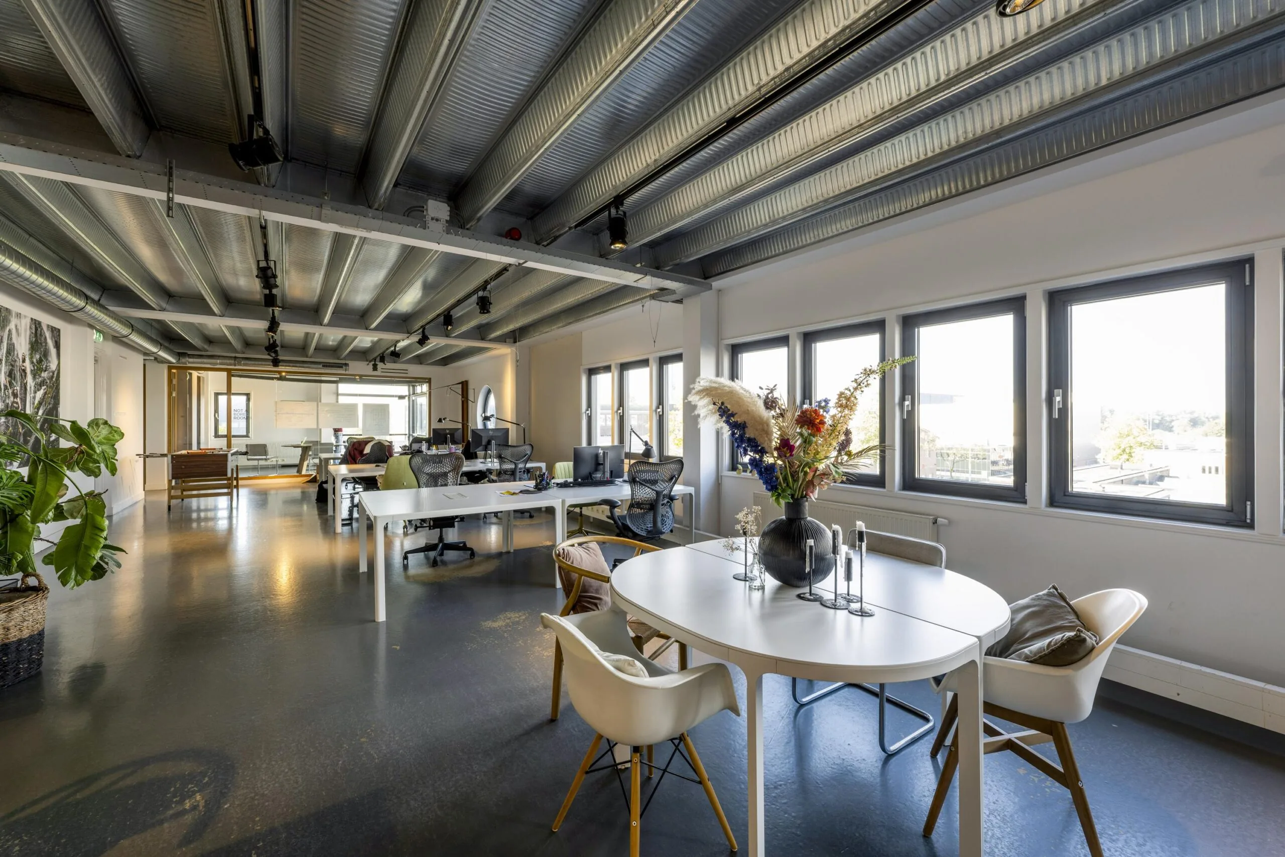 Modern open office space on Helicopterstraat with industrial ceiling, large windows, and minimalist furnishings.